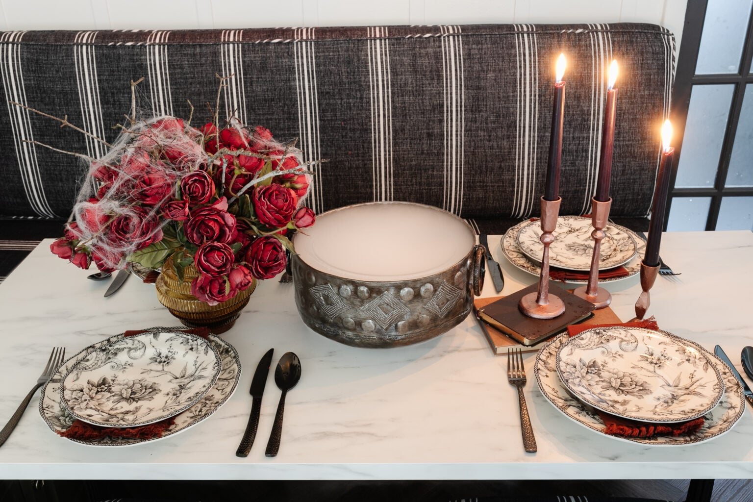 Halloween table decor with bowl of dry ice fog, red roses with spider webs, and black toile dinnerware