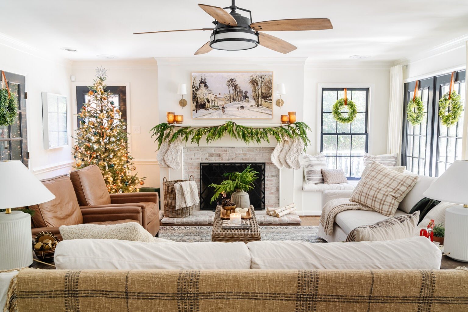 neutral living room christmas with wreaths on windows and realistic garland
