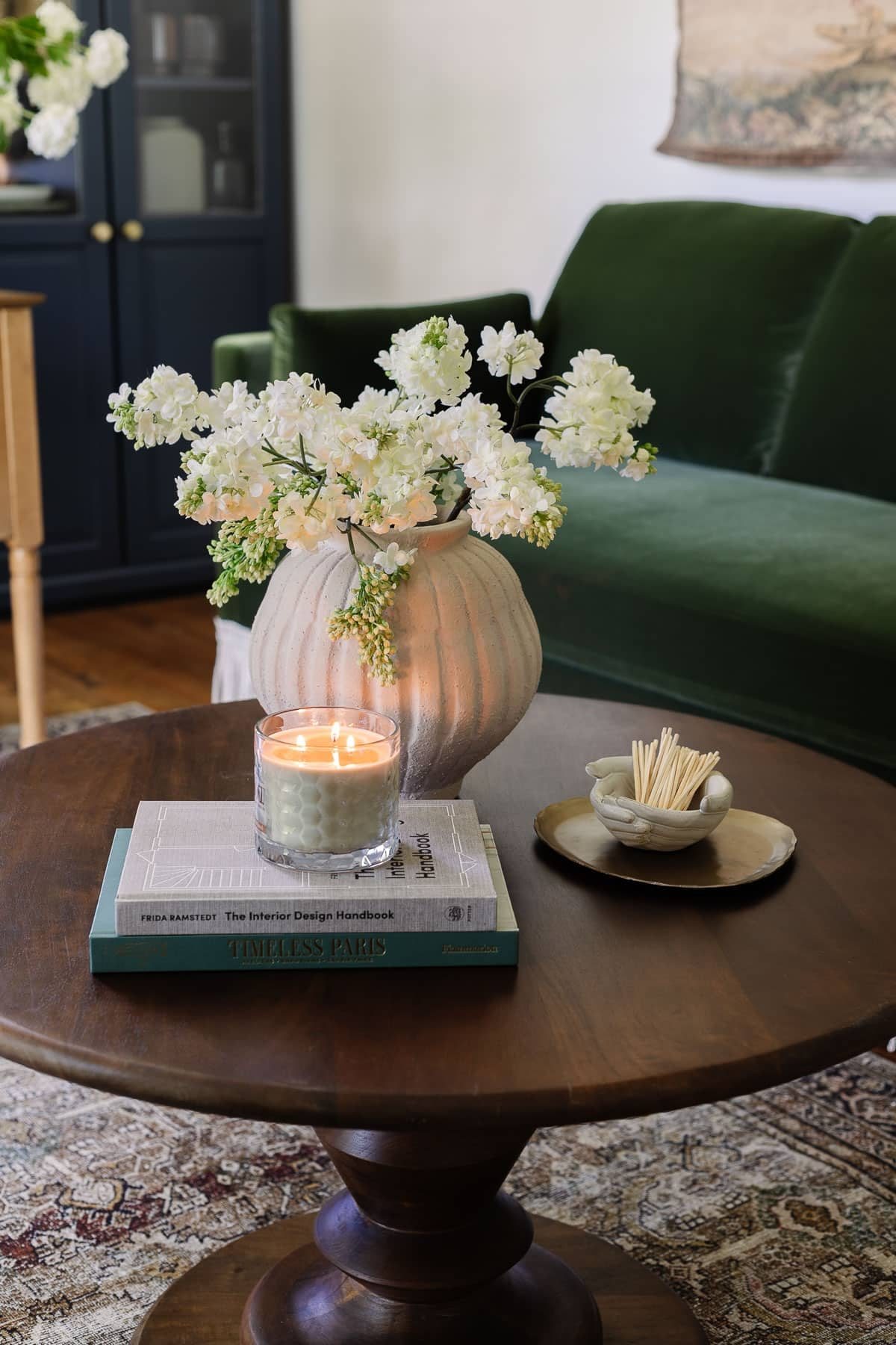coffee table decor with vase of flowers, coffee table books, candle, tray, and bowl of matches