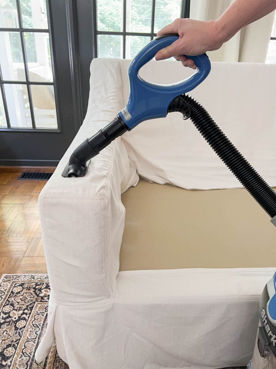 vacuuming sofa slipcover with wand attachment to remove hair, dirt, and lint