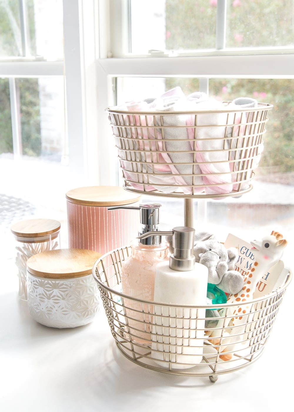 Nursery Organization | Use a tiered fruit basket from the kitchenware aisle to store baby washcloths, grabby toys, Wubbanubs, lotion, and hand sanitizer.