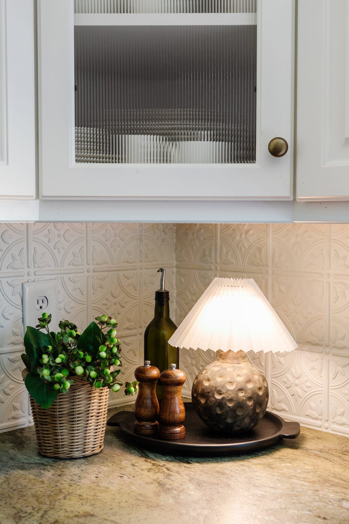 battery operated mini lamp on a kitchen countertop with pleated shade, black tray, and plant