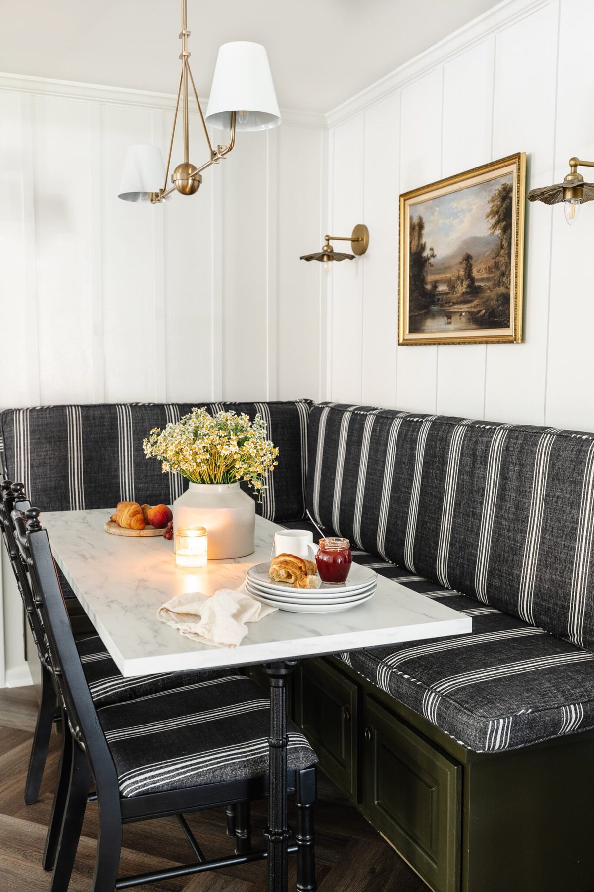 charcoal striped booth in a corner breakfast nook with brass chandelier and wall sconces and marble dining table