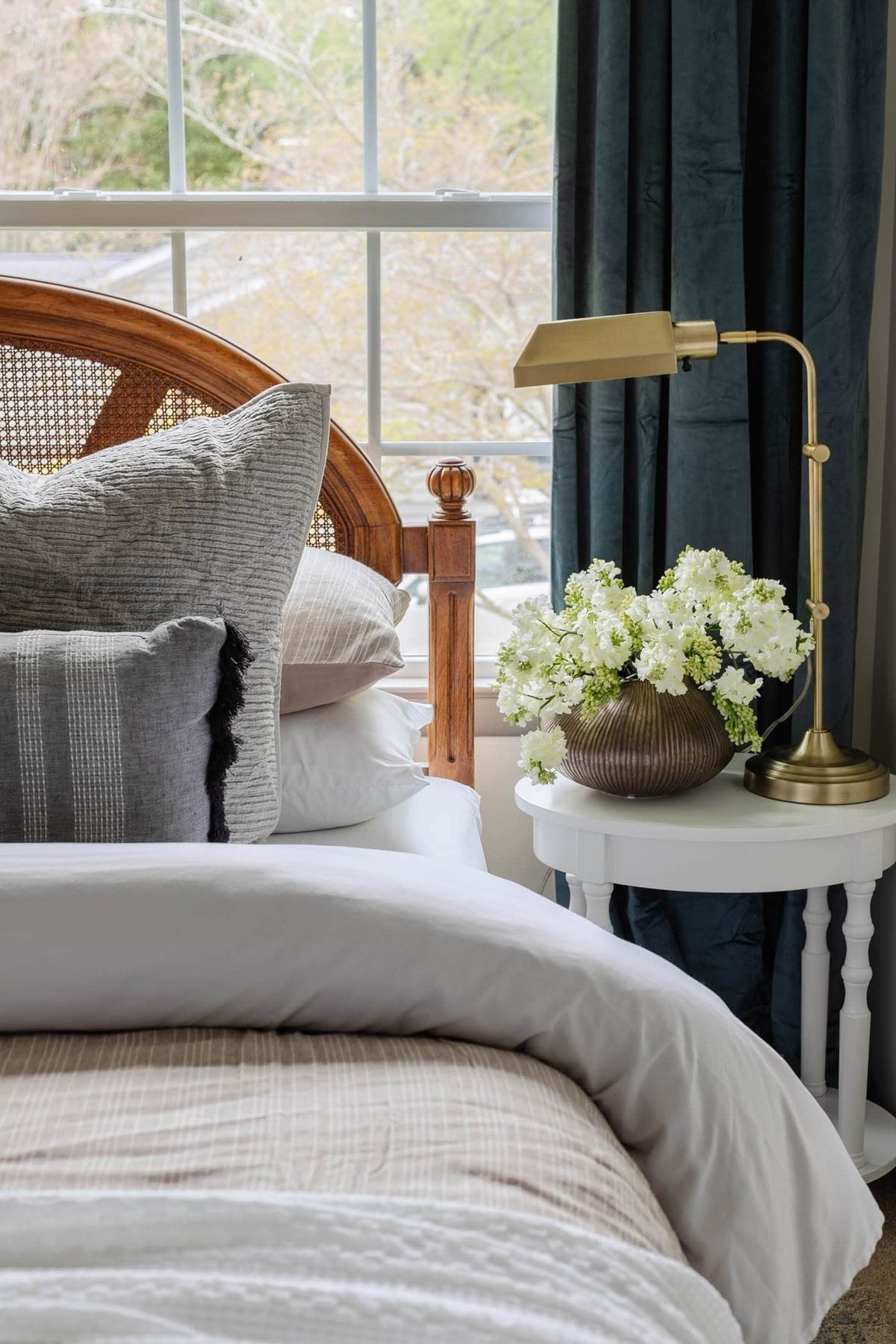 nightstand decor with vase of flowers and lamp in a guest bedroom with cane headboard