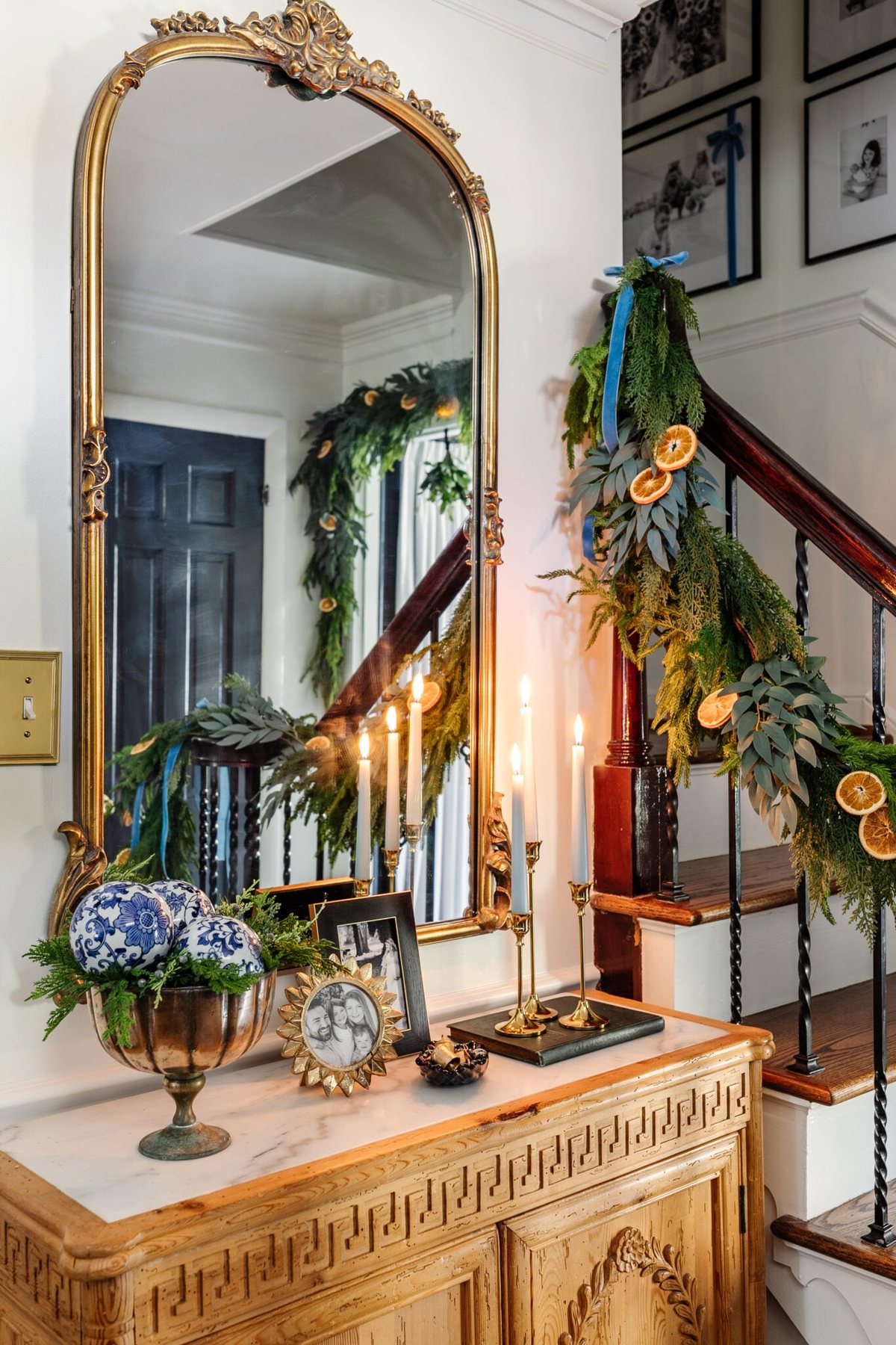 entryway Christmas decor on a table with candles, mirror, picture frames, and bowl of greenery
