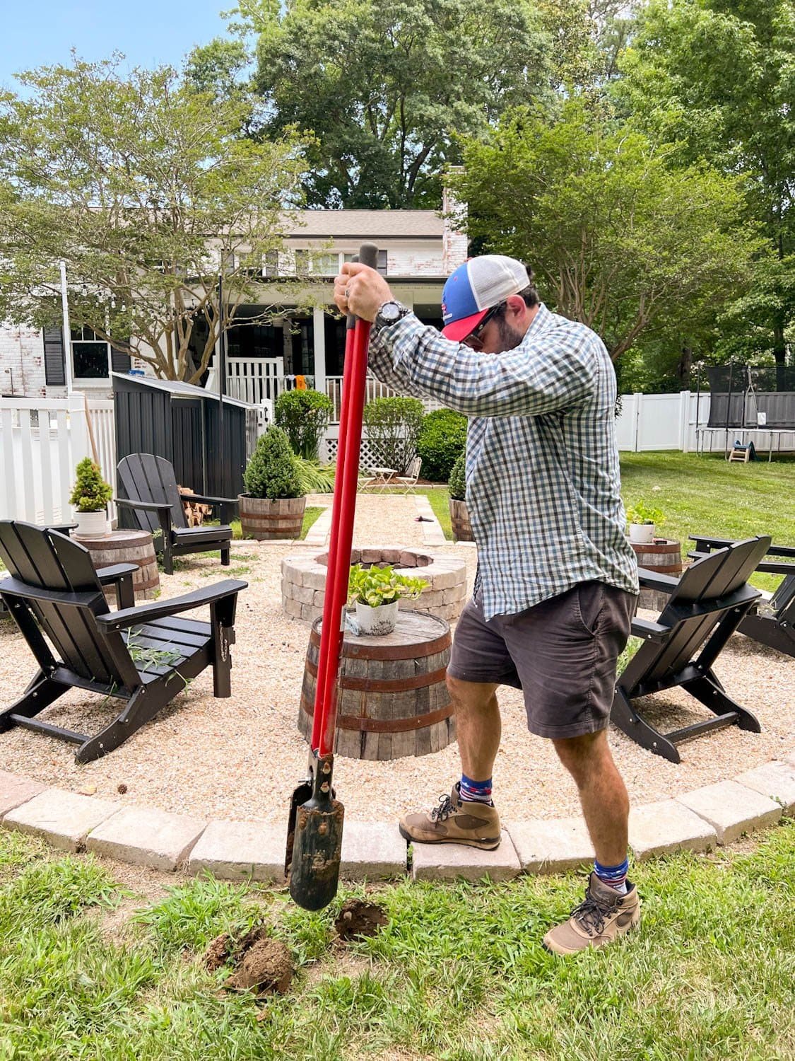 using a post hole digger to dig holes for string light poles around a fire pit