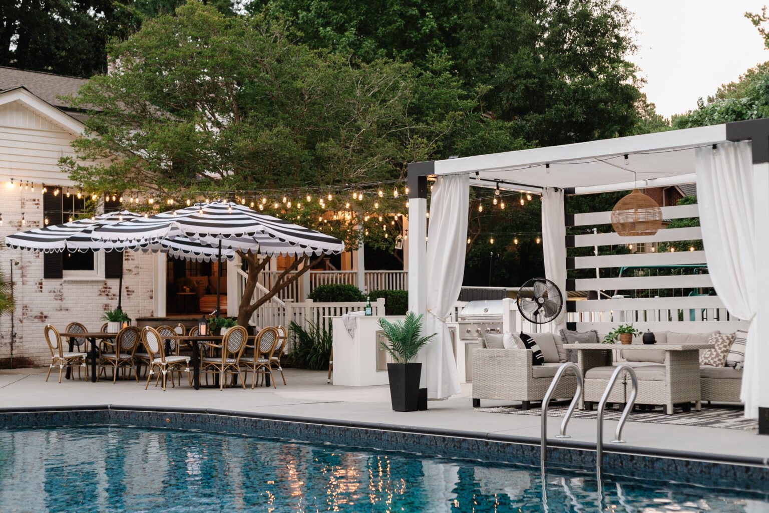 backyard swimming pool with outdoor dining sets, striped umbrella, painted vinyl siding on shed, painted concrete deck, poolside patio furniture and cabana