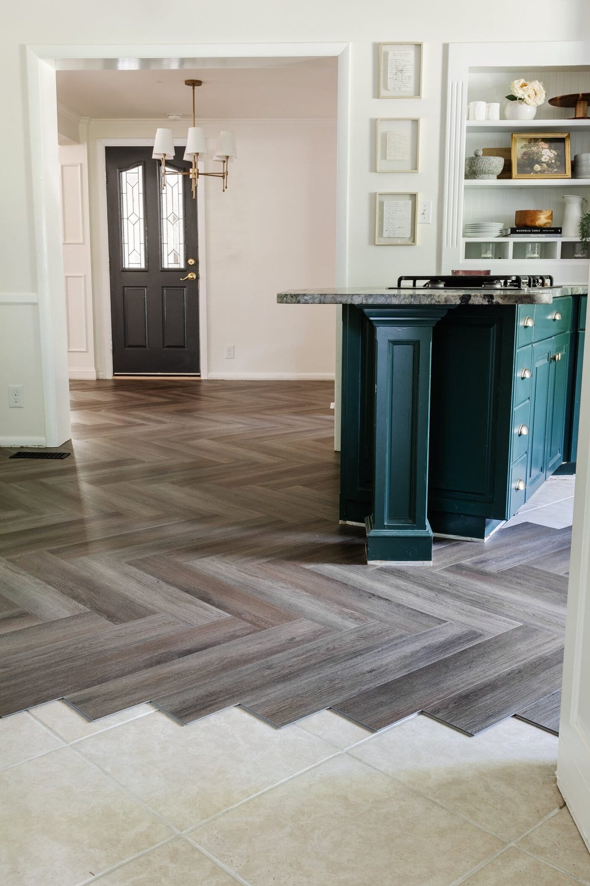 herringbone LVP floating floor over tile in a kitchen with white and green cabinets