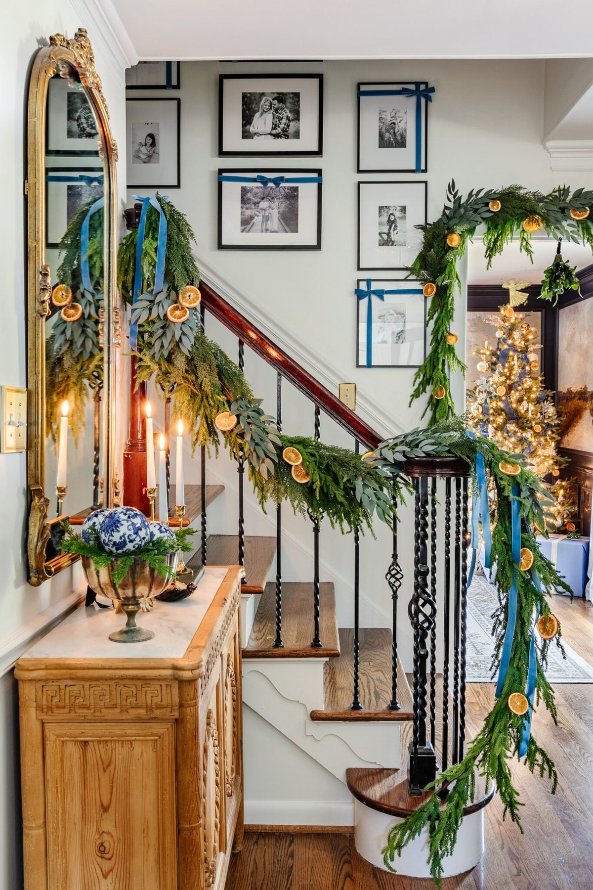 blue and white entryway Christmas decor with staircase garland of greenery, dried oranges, and blue ribbon