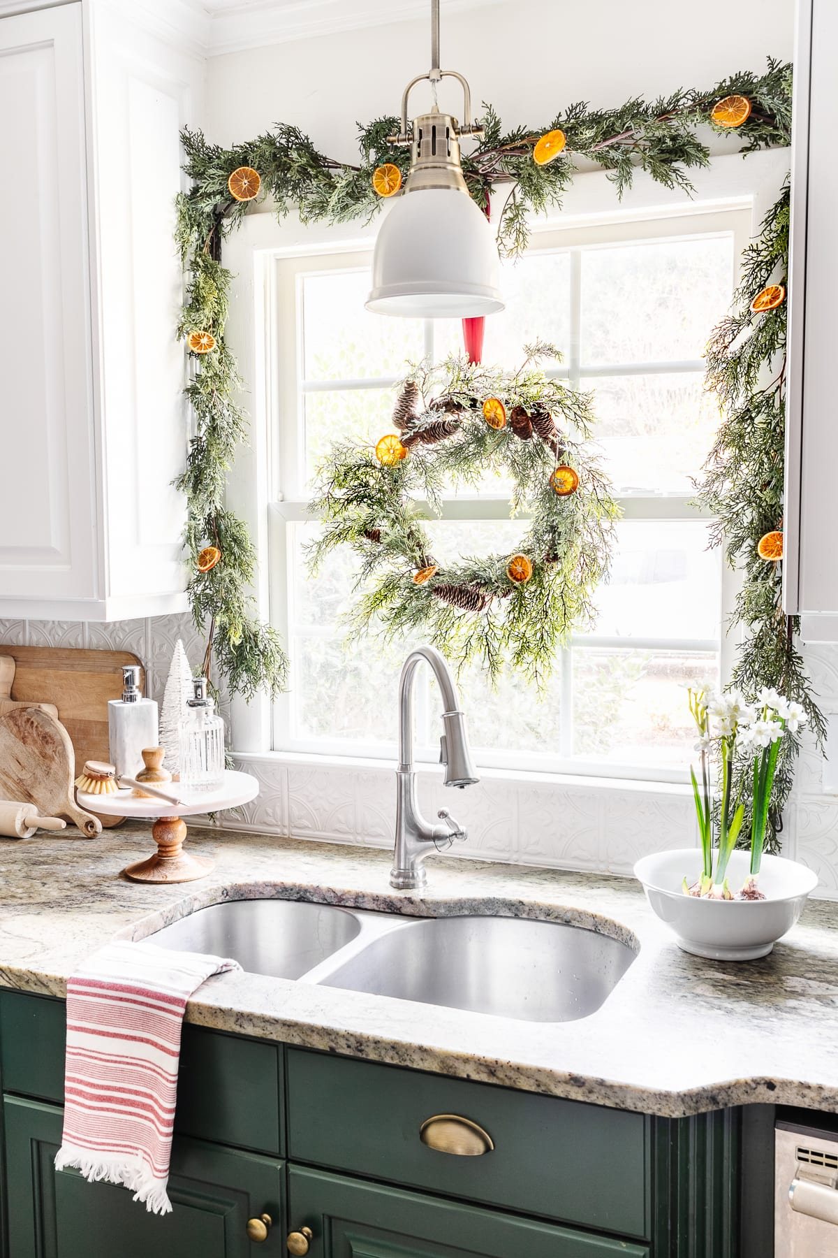 bowl of paperwhite flowers beside a kitchen sink with garland and Christmas wreath on a window