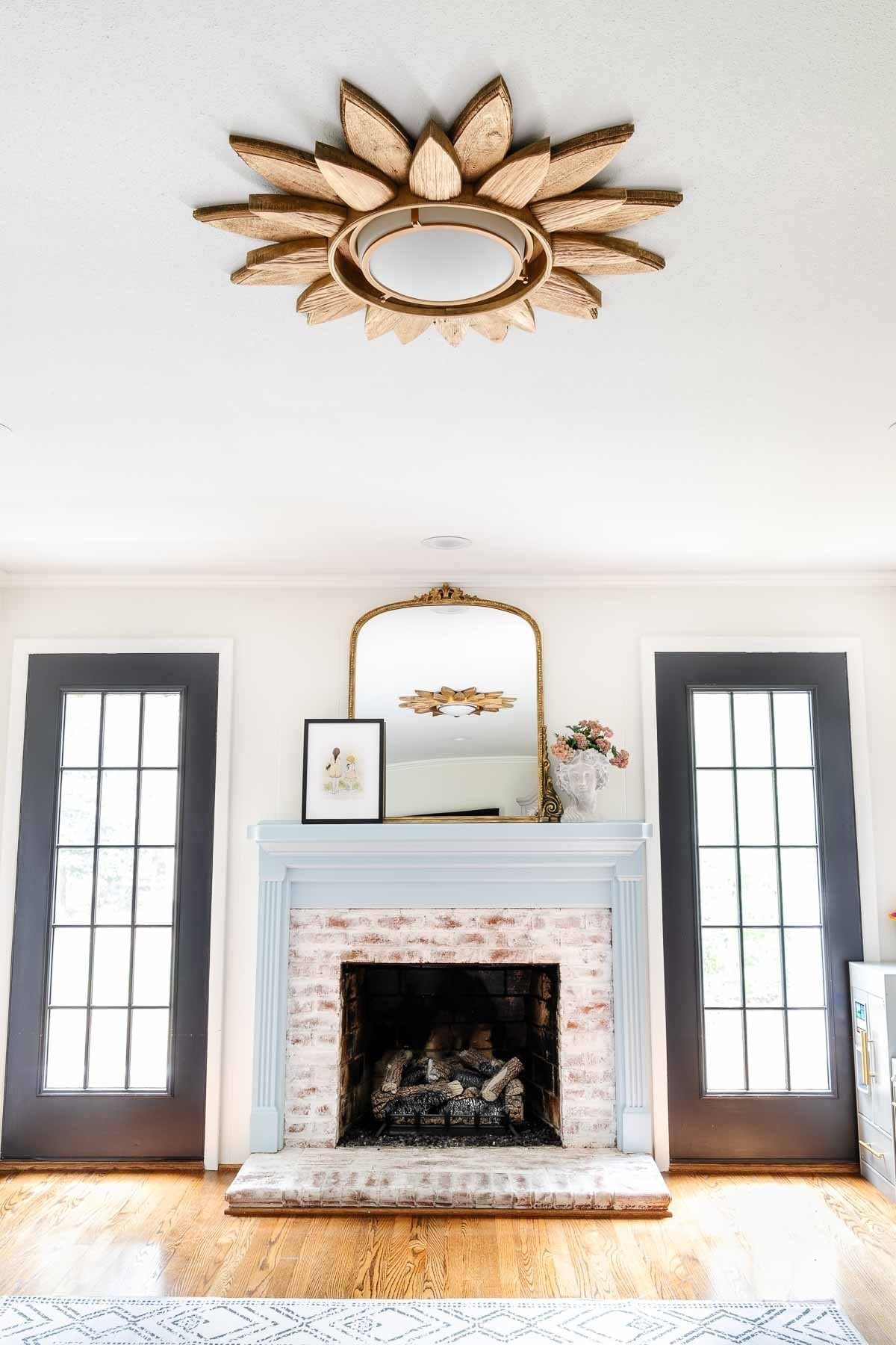 white playroom with black French doors and light blue mantel styled with a mirror and bust planter and sunburst light fixture