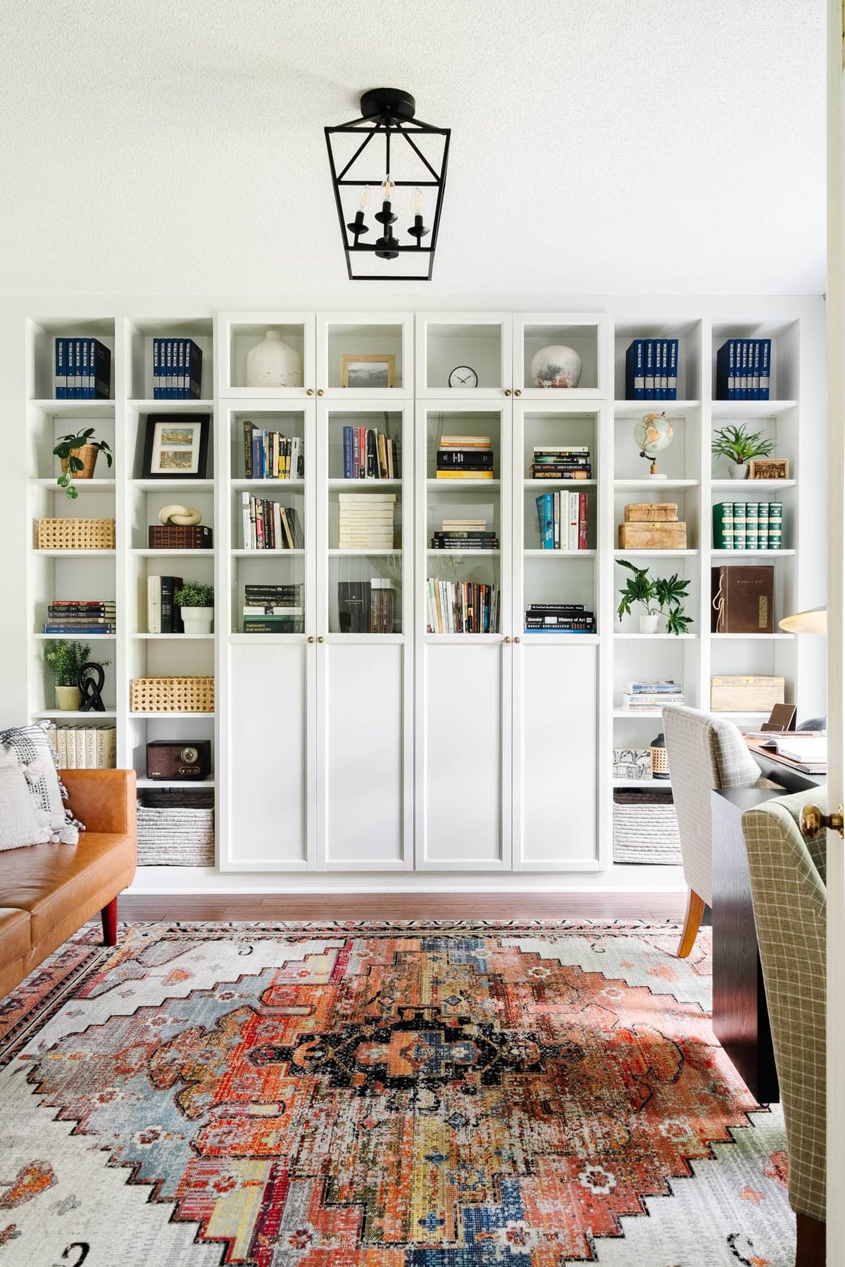 home office with white built-in bookshelves and glass front cabinets, futon, rug, and desk against a window