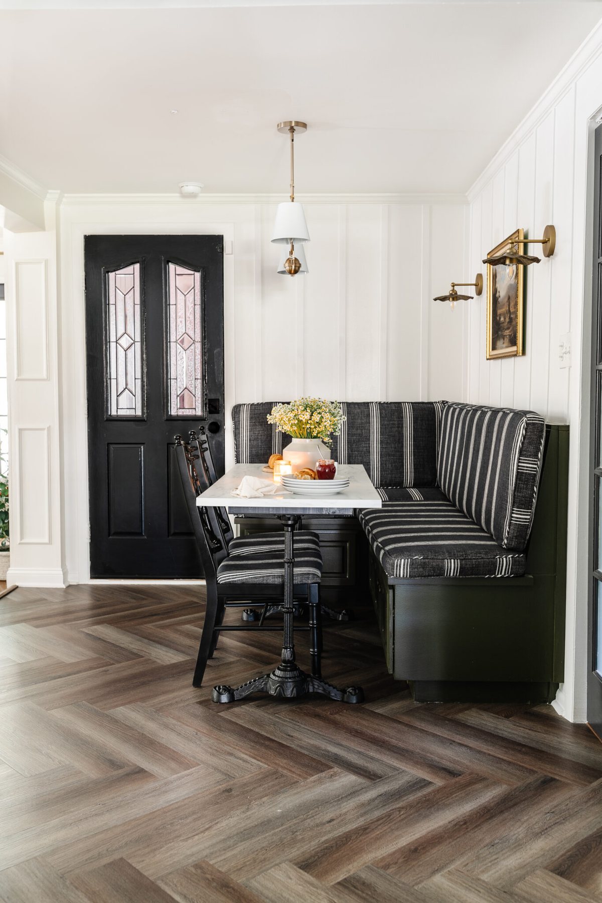 breakfast nook with striped banquette bench, marble bistro dining table, white batten walls, and herringbone LVP flooring
