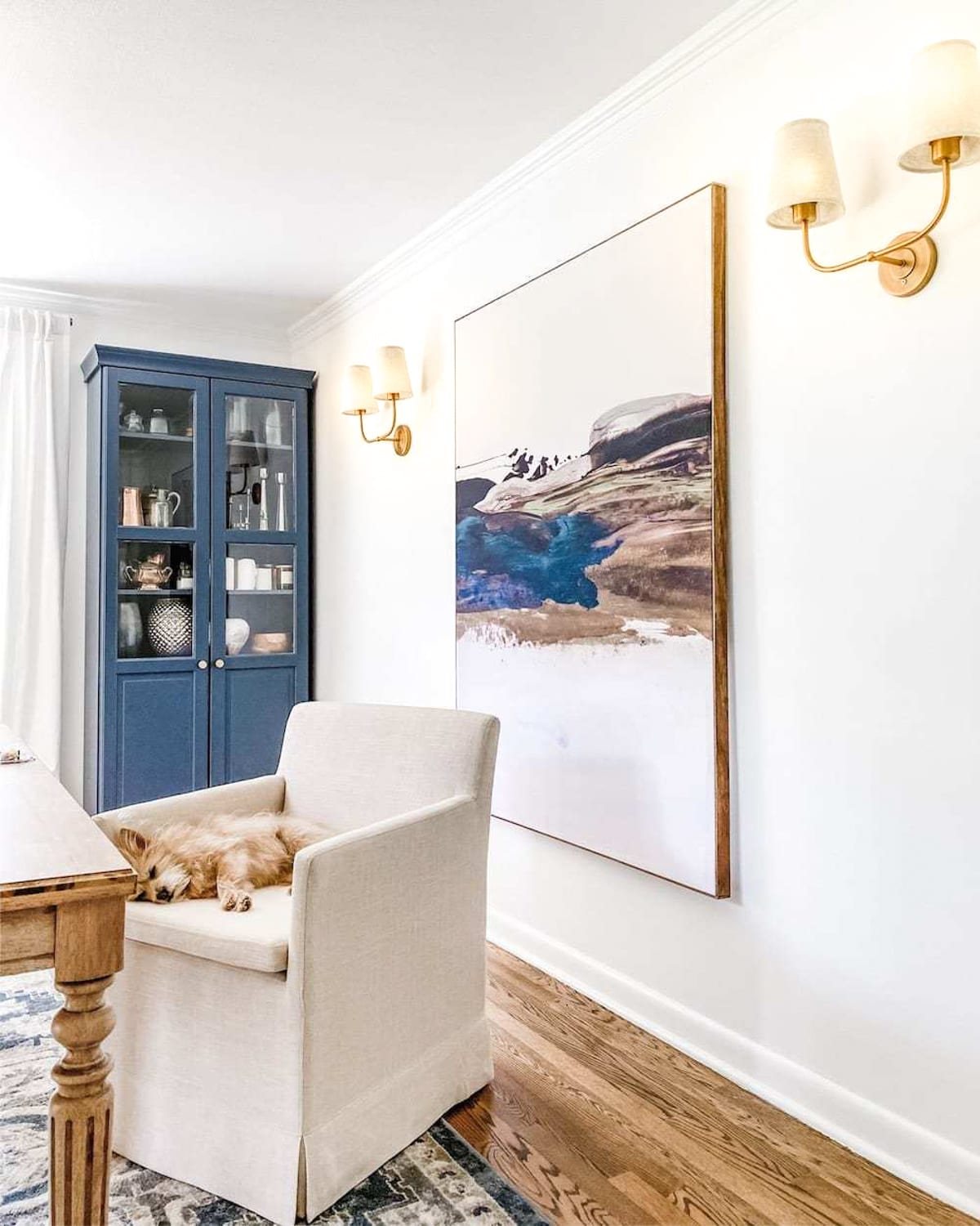 double shaded vintage wall sconces in a home office with oversized art, rolling chair, and navy cabinet