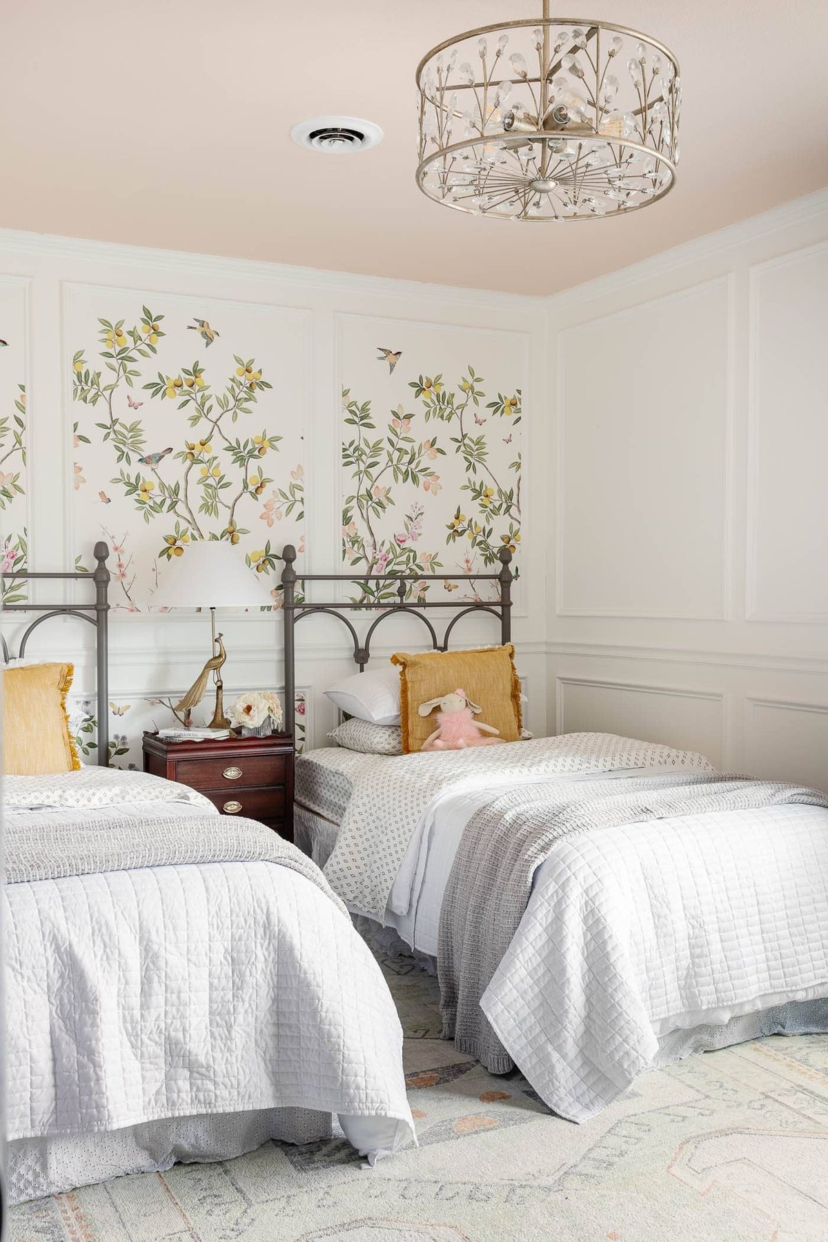 cottagecore girl's bedroom with blush pink ceiling, chinoiserie wallpaper, vintage twin beds, wood furniture, and picture frame molding