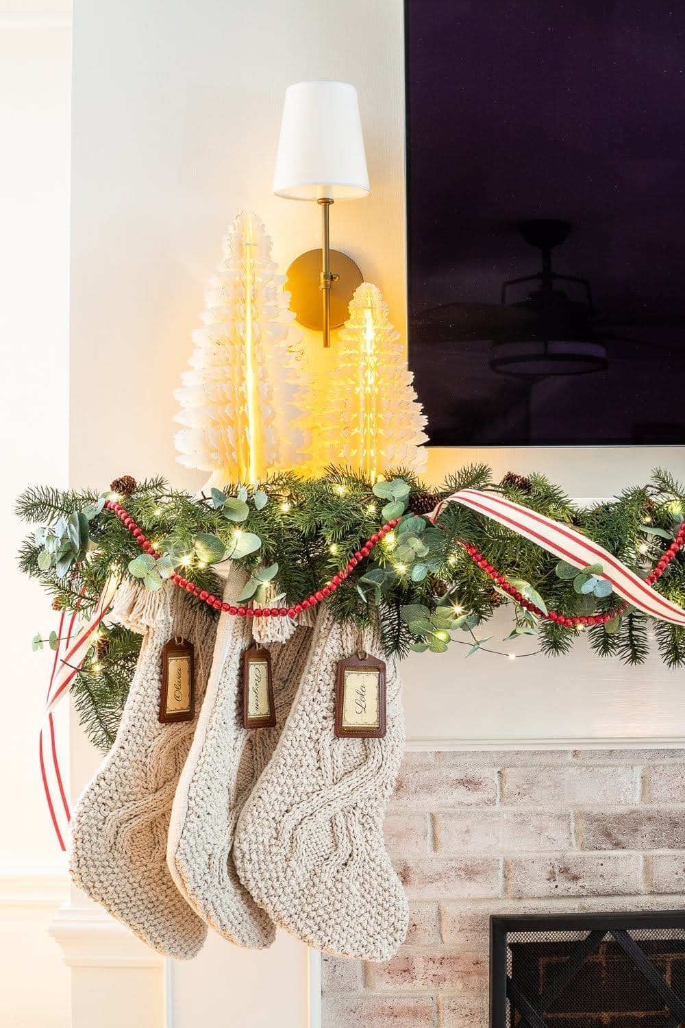 Swedish Christmas with paper tree figurines, chunky knit stockings, abundant greenery, fairy lights, and pops of red