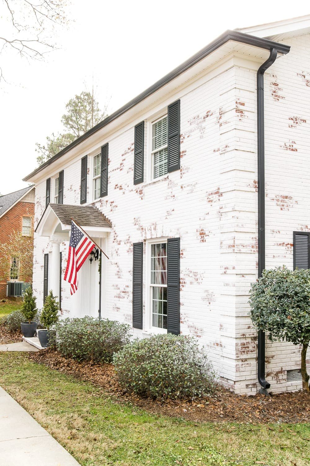 white brick colonial house with black shutters and black gutters