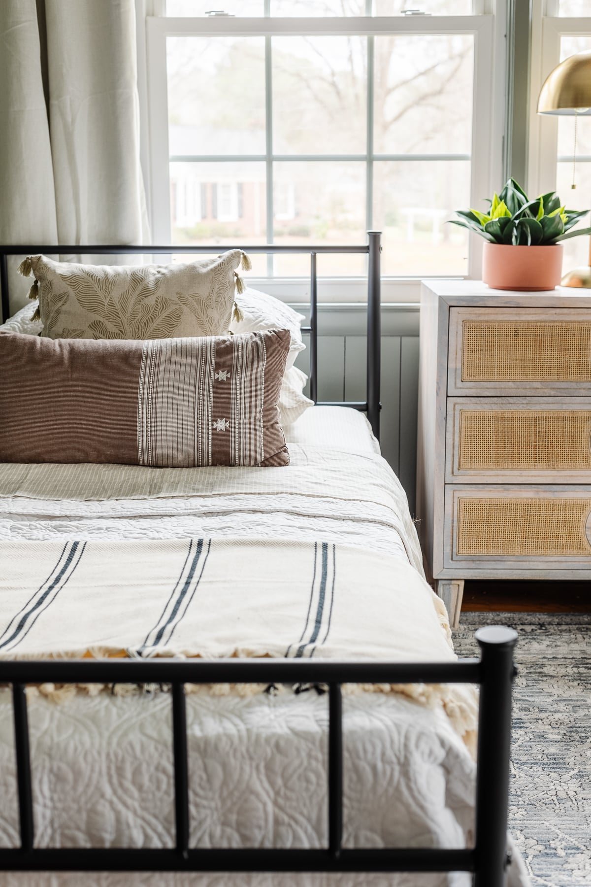 twin bed and rattan nightstand chest in front of a window