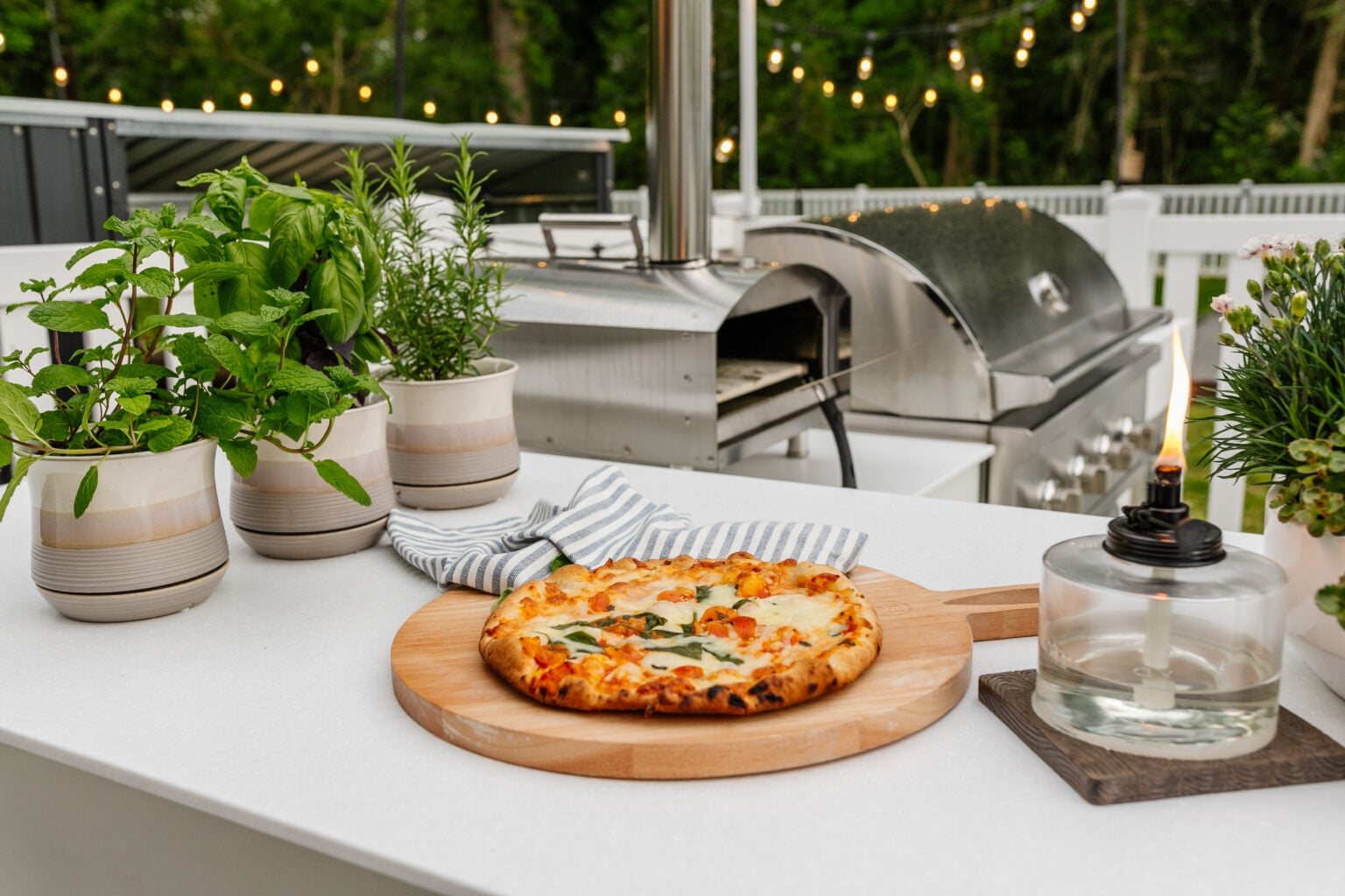 backyard grill with outdoor pizza oven, tabletop tiki torch, and potted herbs
