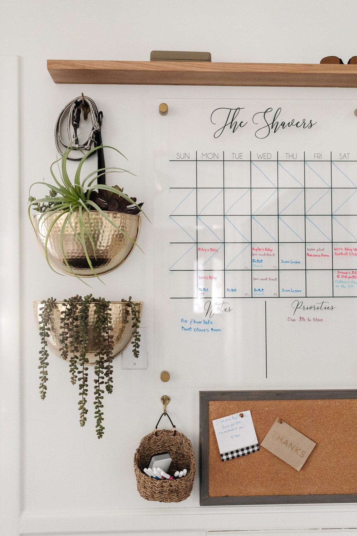 family command center with wall calendar, brass planters, shelf, and memo board