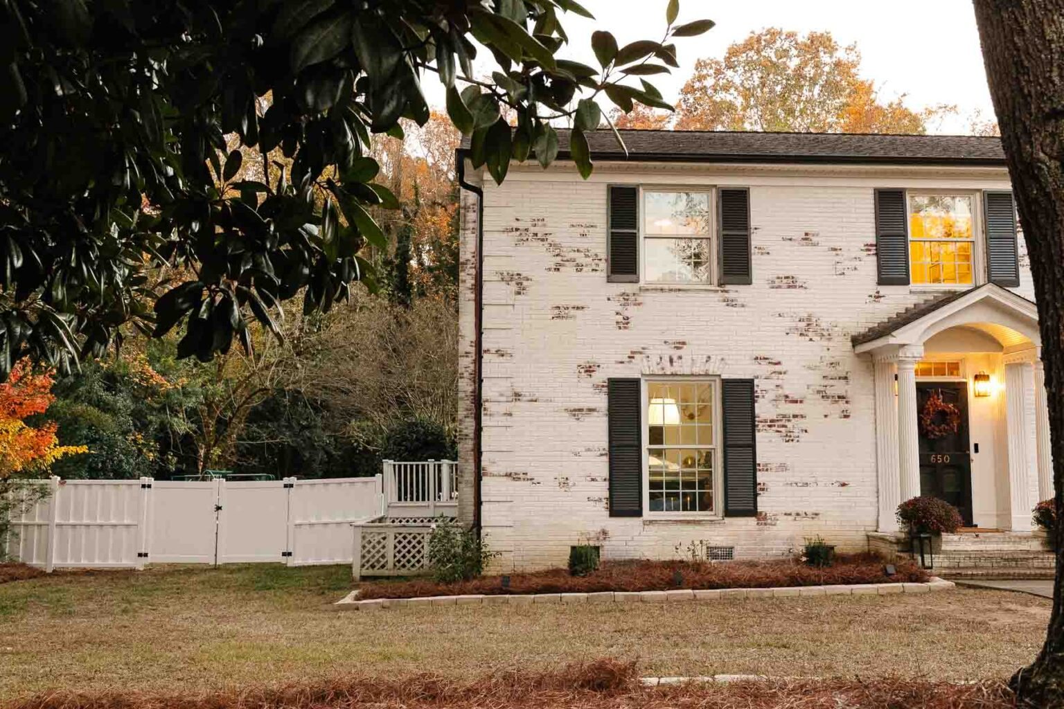 white limewashed brick colonial house with backyard fence