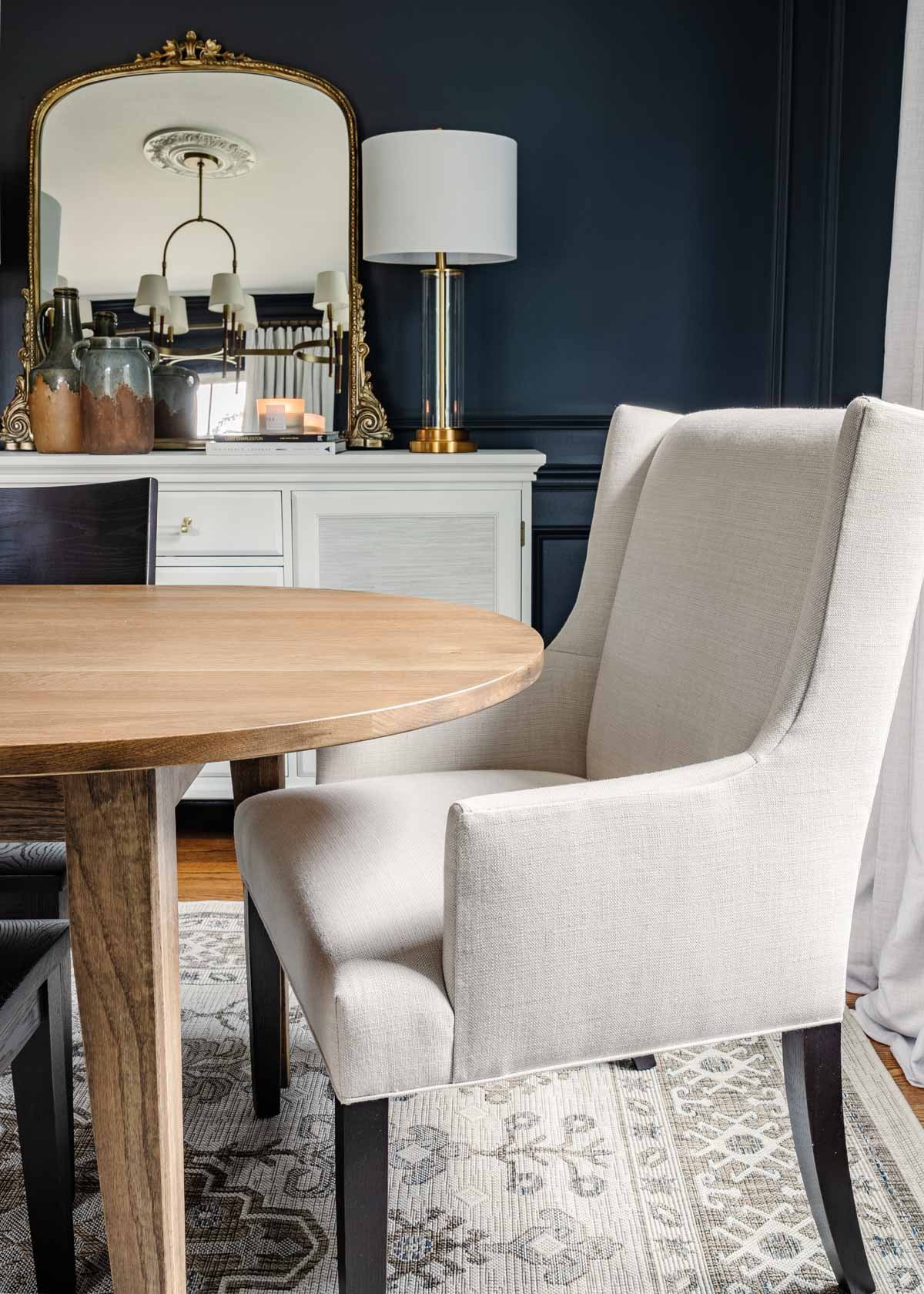 midcentury modern dining table with upholstered chairs, navy walls, and french mirror