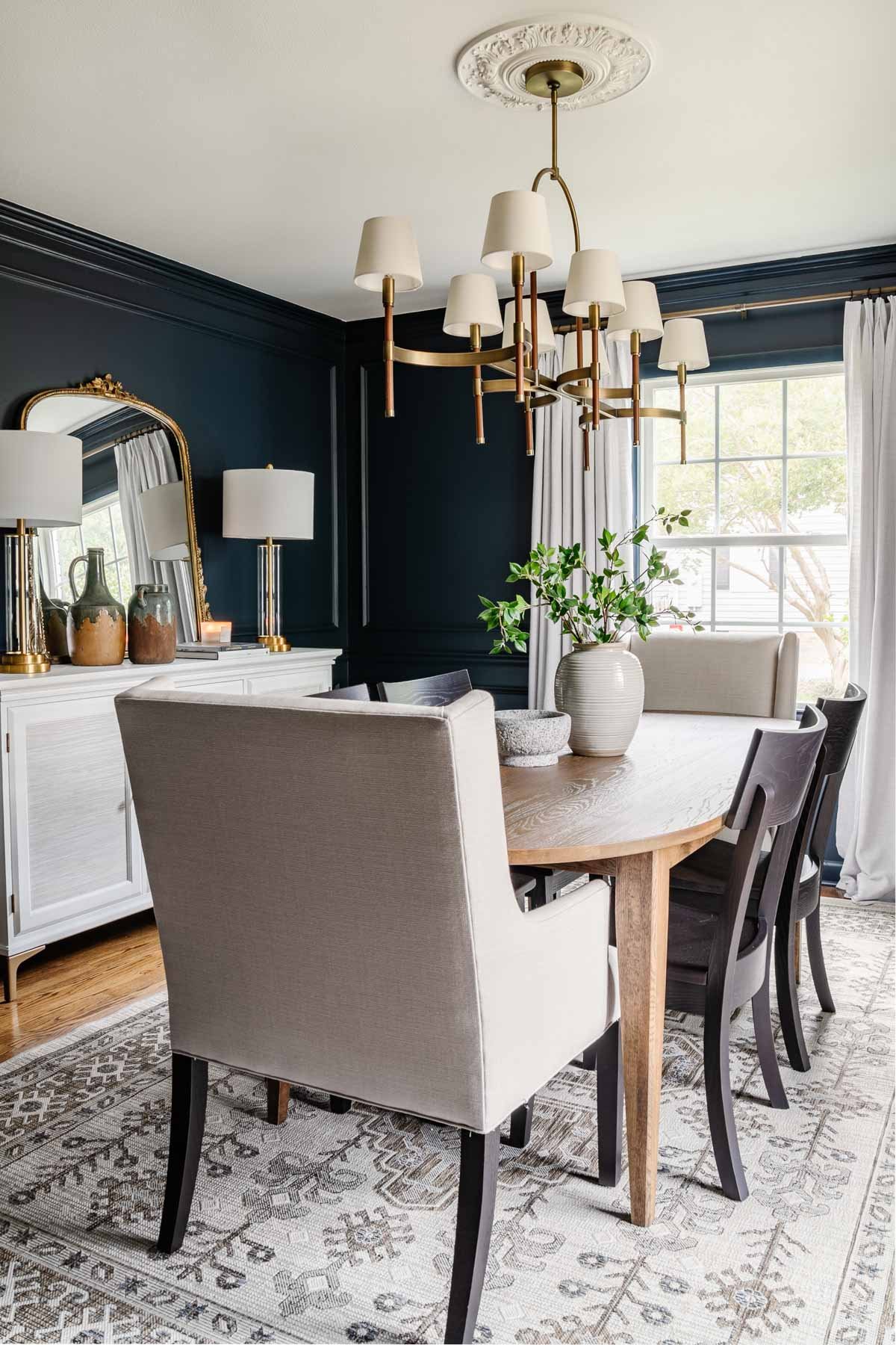 classic modern dining room with mid century modern dining table, navy walls, black chairs, French mirror, and white buffet