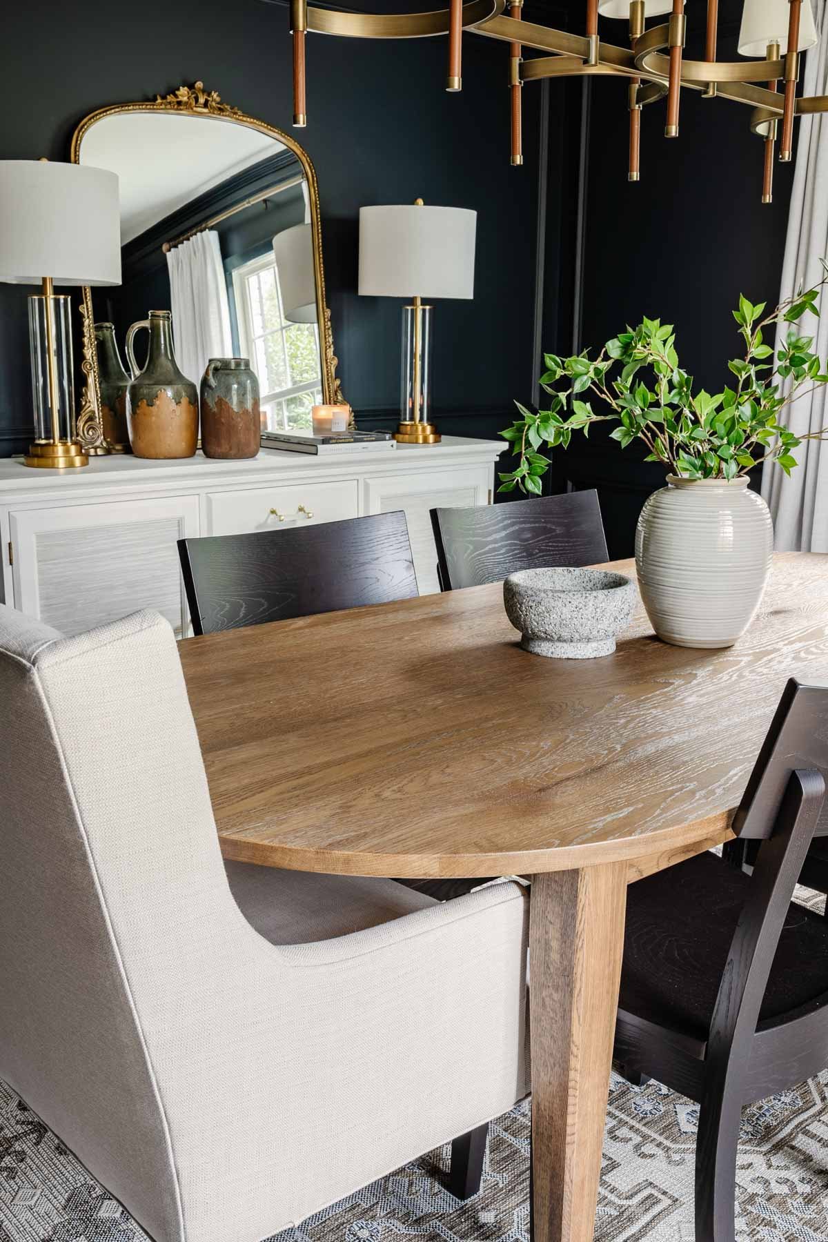 classic modern dining room with navy walls, linen curtains, wood MCM table, black chairs, and French mirror