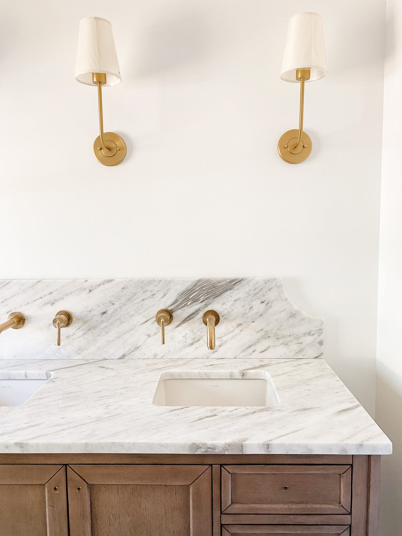 scalloped marble backsplash with gold wall mount faucets in en suite bathroom