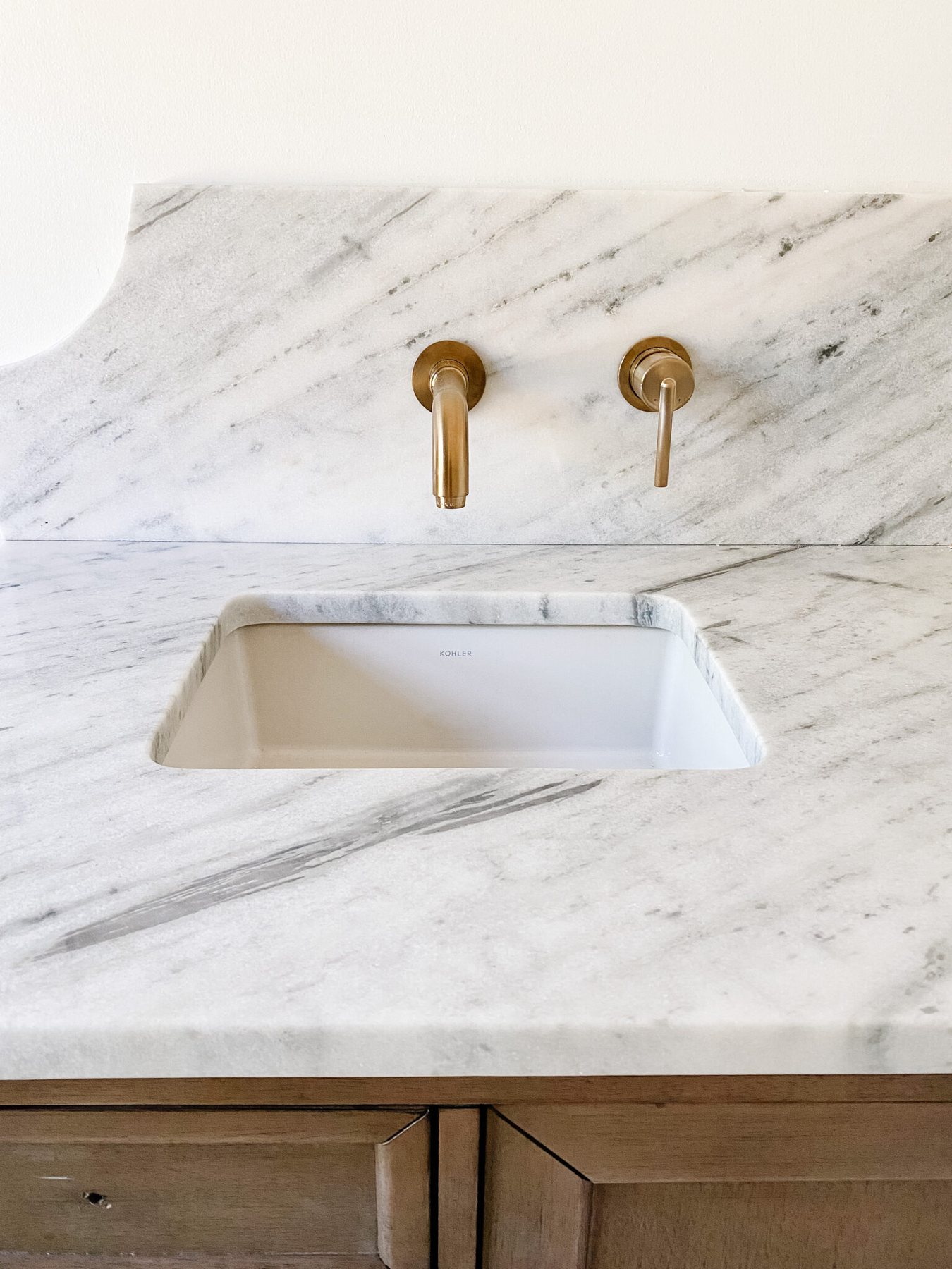 scalloped marble backsplash with gold wall mount faucets in en suite bathroom