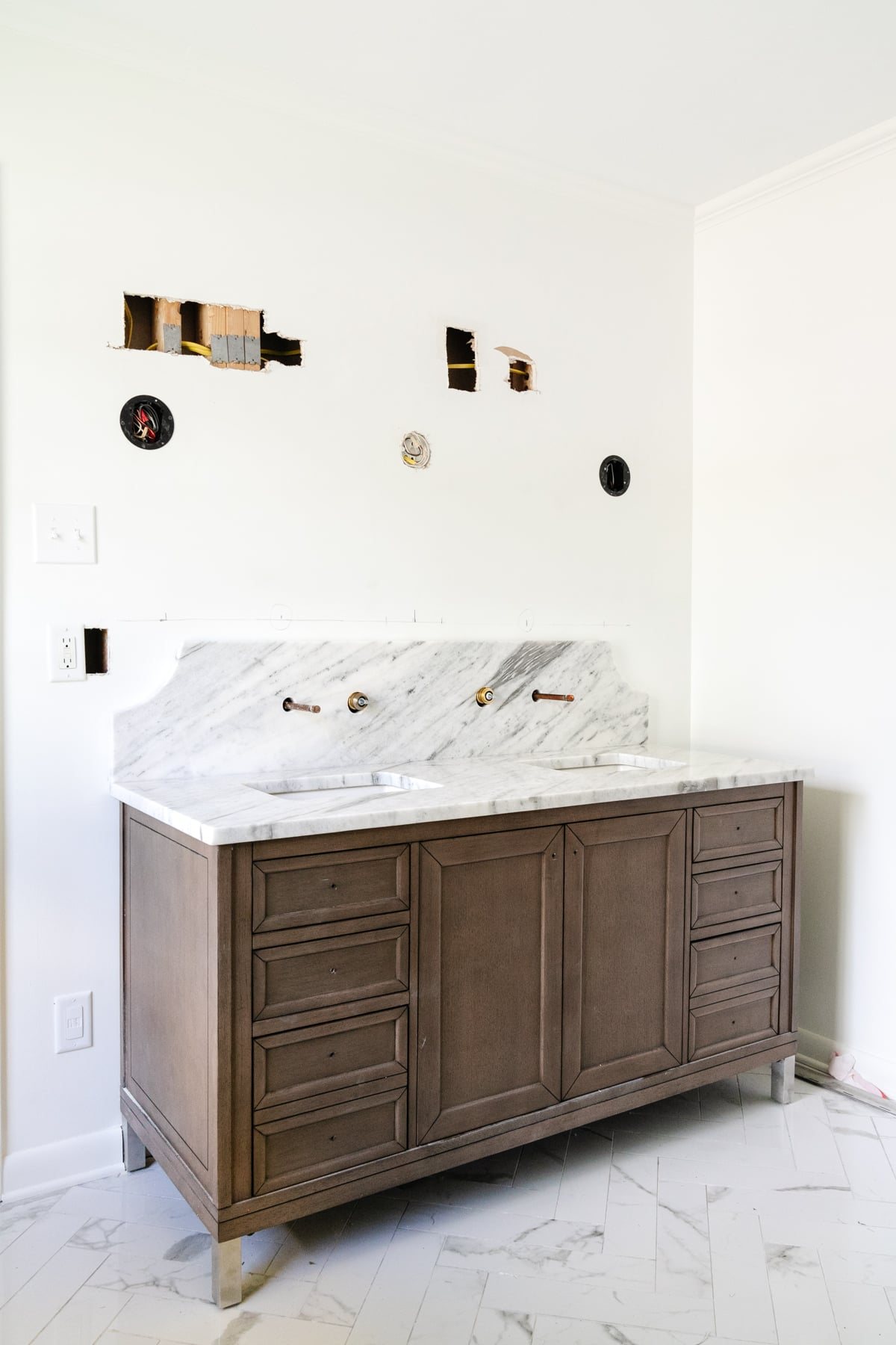 wood double vanity in a bathroom with scalloped marble backsplash and herringbone tile floor