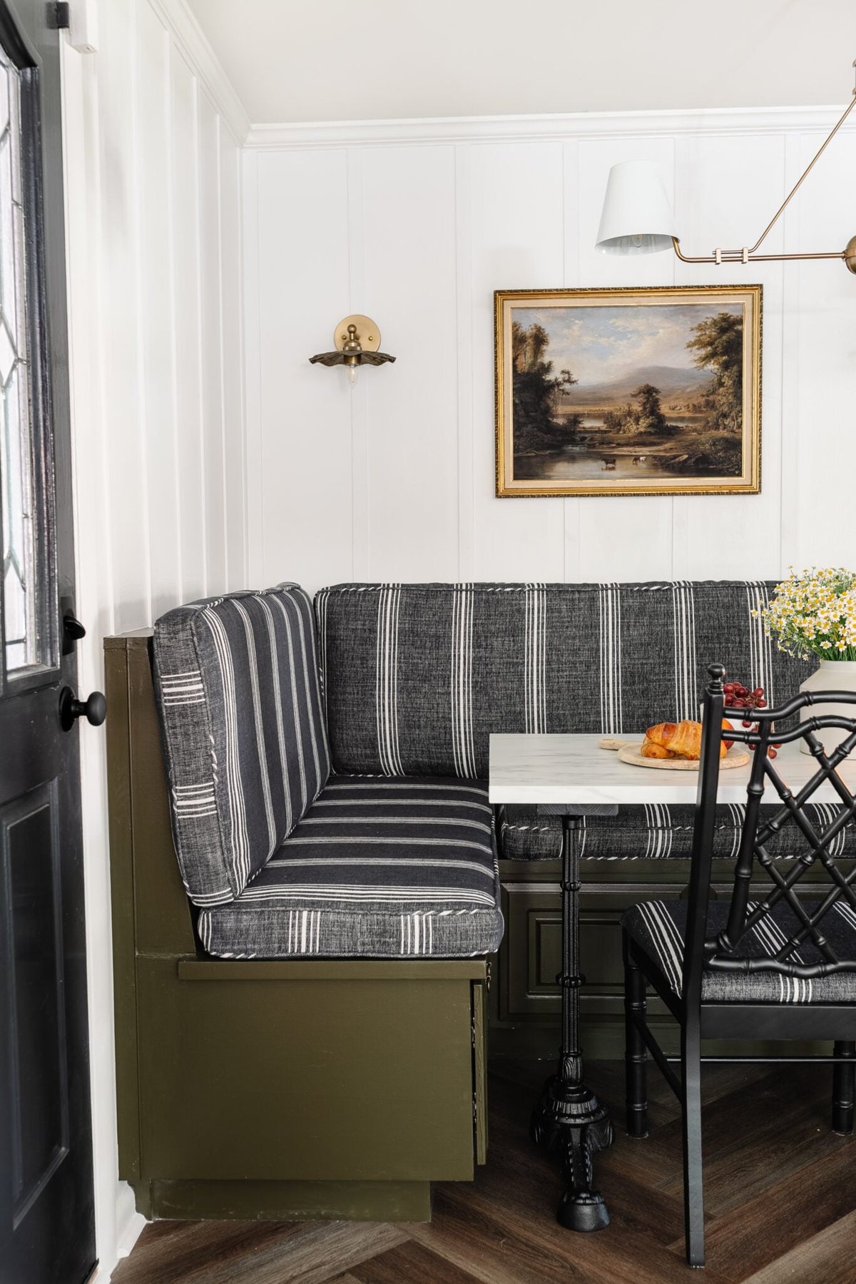 striped charcoal cushions on a banquette bench painted olive green with white batten walls and an antique landscape oil painting