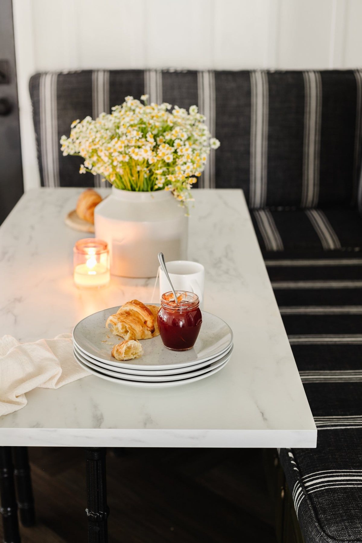 marble dining table top with plates stacked and vase of daisy flowers