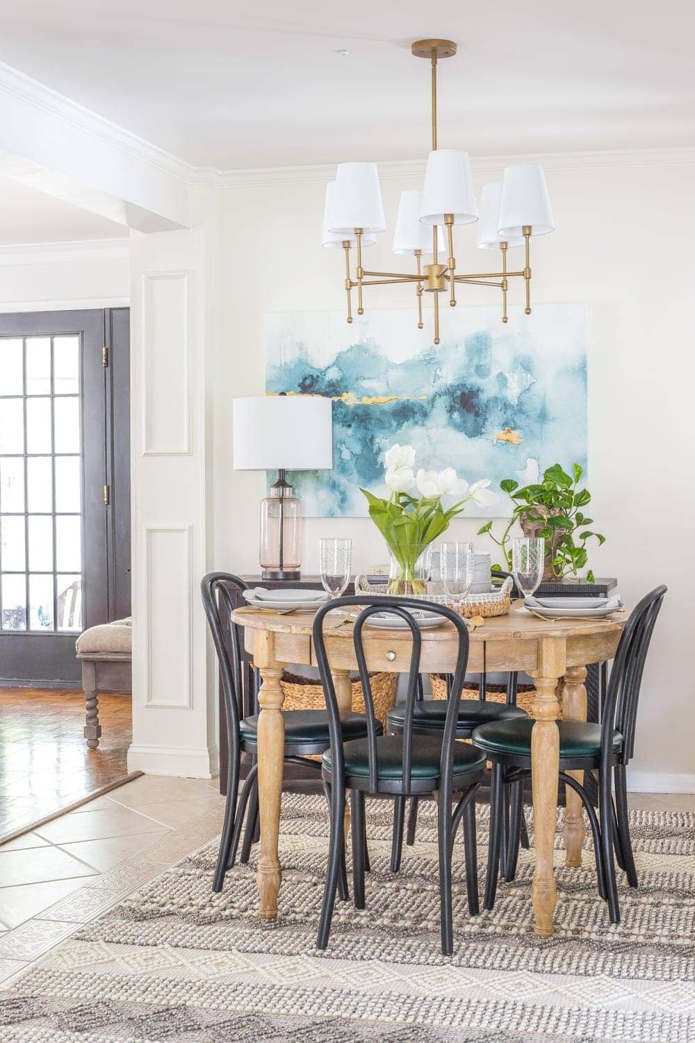 small dining room with black bentwood chairs, wood dining table, blue watercolor art, and brass shaded chandelier
