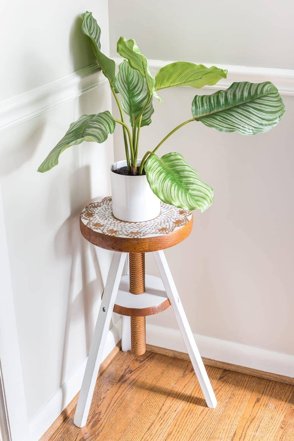 A global designer-inspired DIY plant stand made from a thrifted piano stool using just spray paint and a doily for a quick and easy makeover. #plantstand #pianostool #globaldecor #spraypaint #thriftstoreflips #thrifting #diyhomedecor #thriftedhomedecor