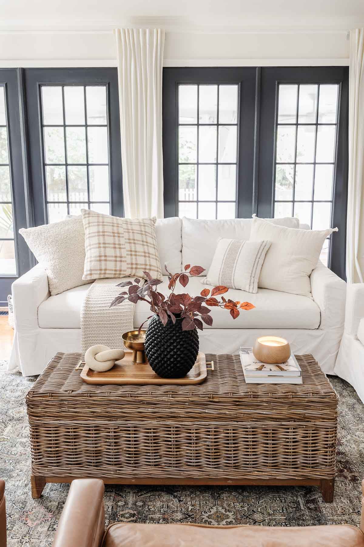 coffee table decor ideas with rattan coffee table trunk, black vase with fall stems, wooden candle, coffee table books, wooden tray, brass bowl, and stone knot sculpture