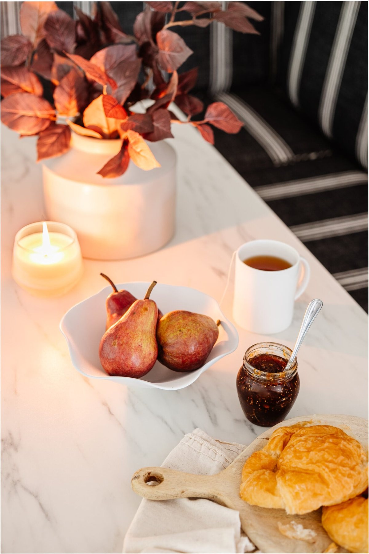 white ruffled bowl on a dining table with pears and vase of fall branches
