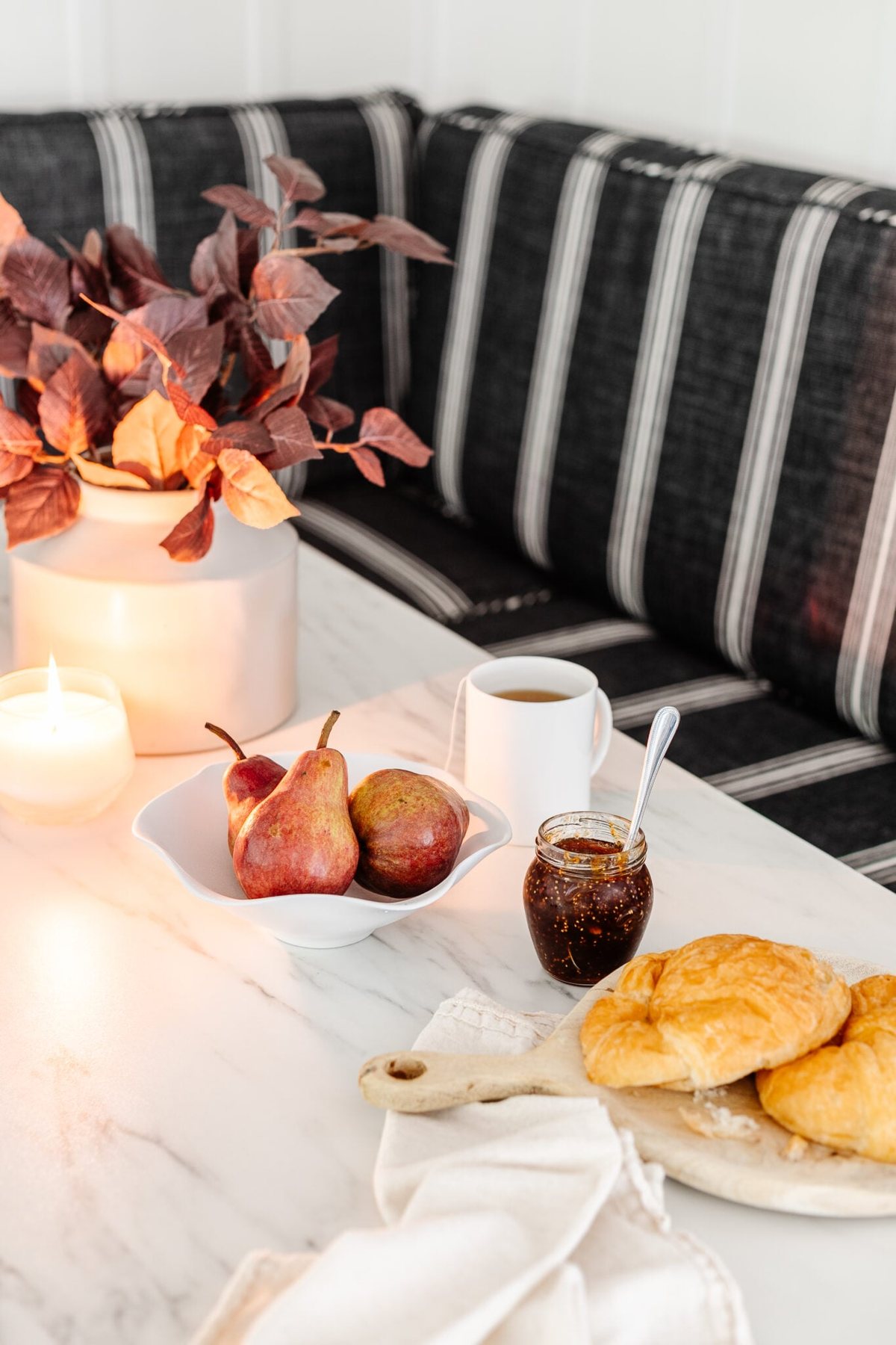 scalloped bowl on a dining table with pears, jam, and croissants