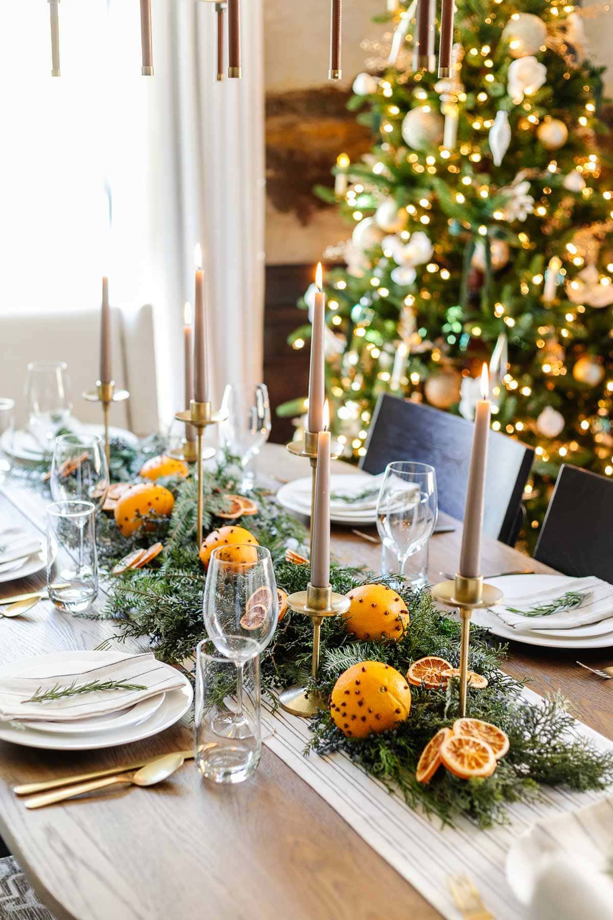 simple christmas table centerpiece using dried orange slices, orange pomanders, candle holders, and fresh evergreen branches