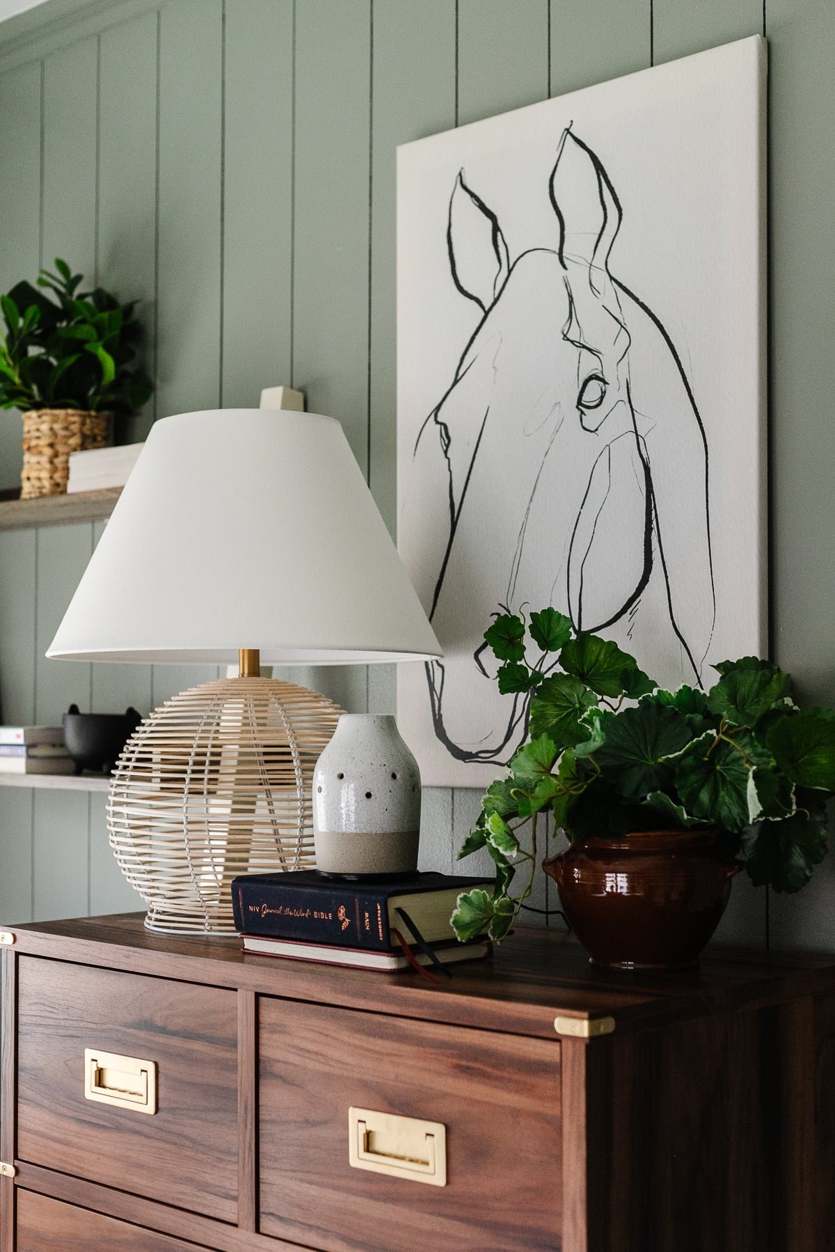 rattan lamp, diffuser, and horse art on top of a dresser