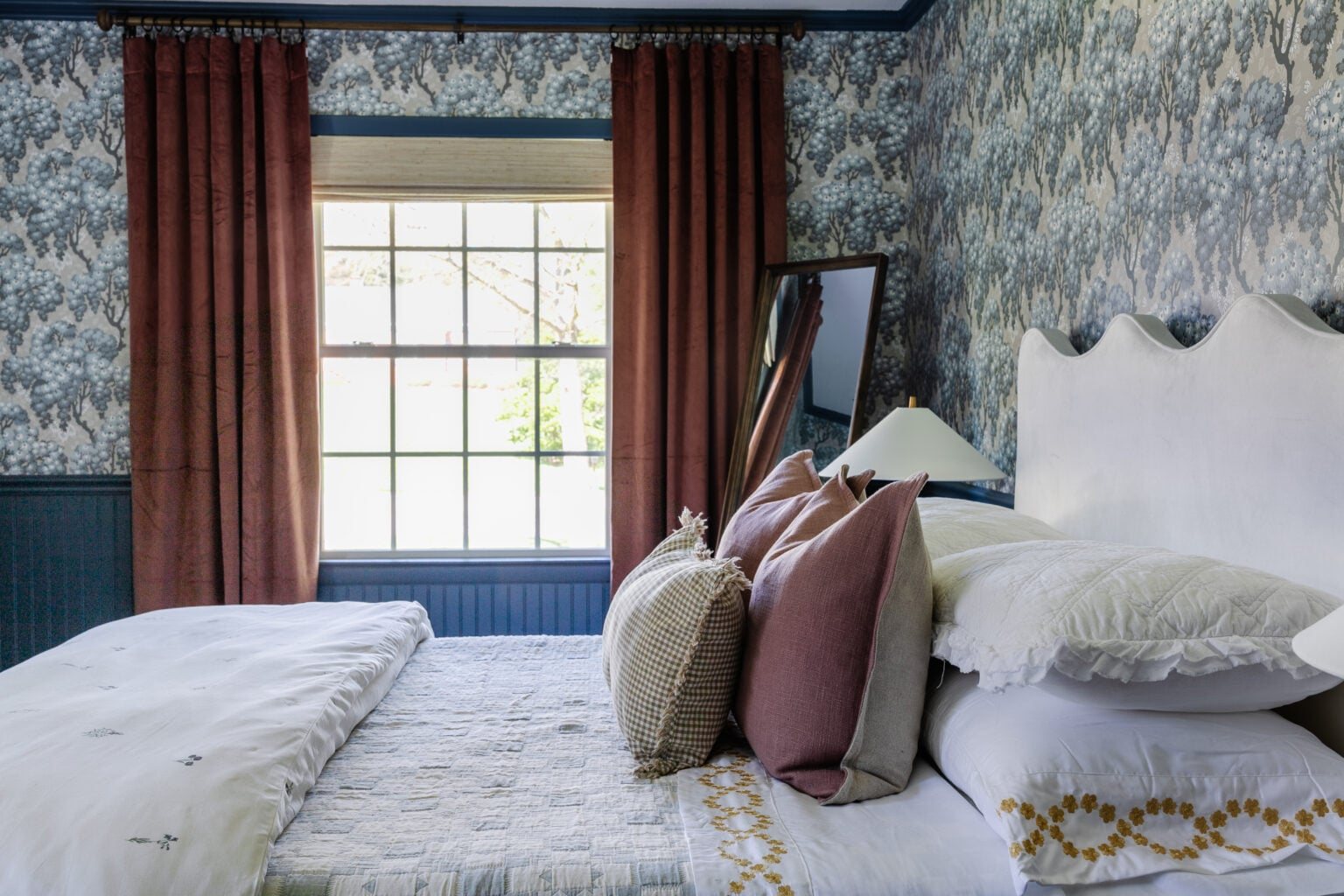 Swedish cottage bedroom with Sandberg Ragnvi floral wallpaper, dusty rose curtains, and vintage quilt