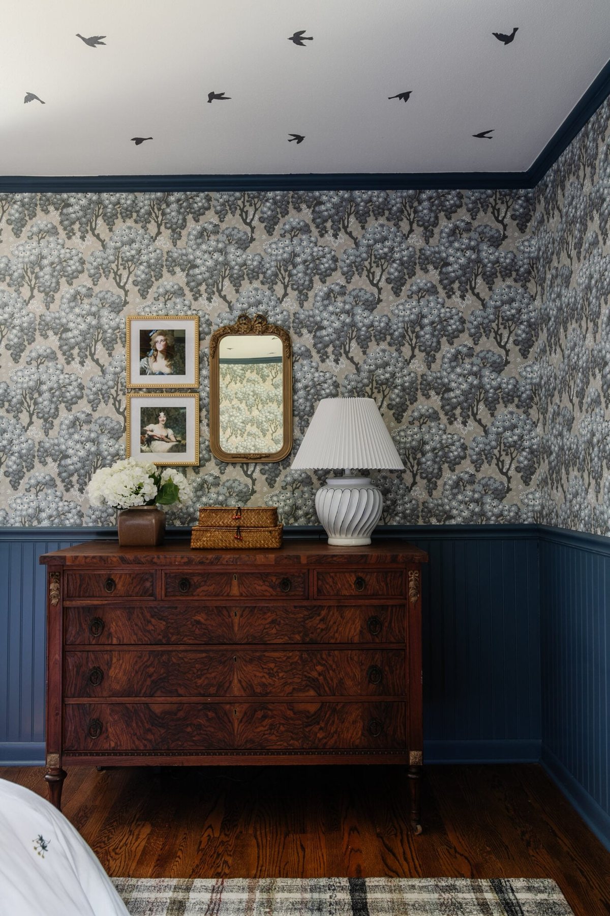 burl wood dresser with swedish cottage style wallpaper and gallery wall with mirror and altered portraits
