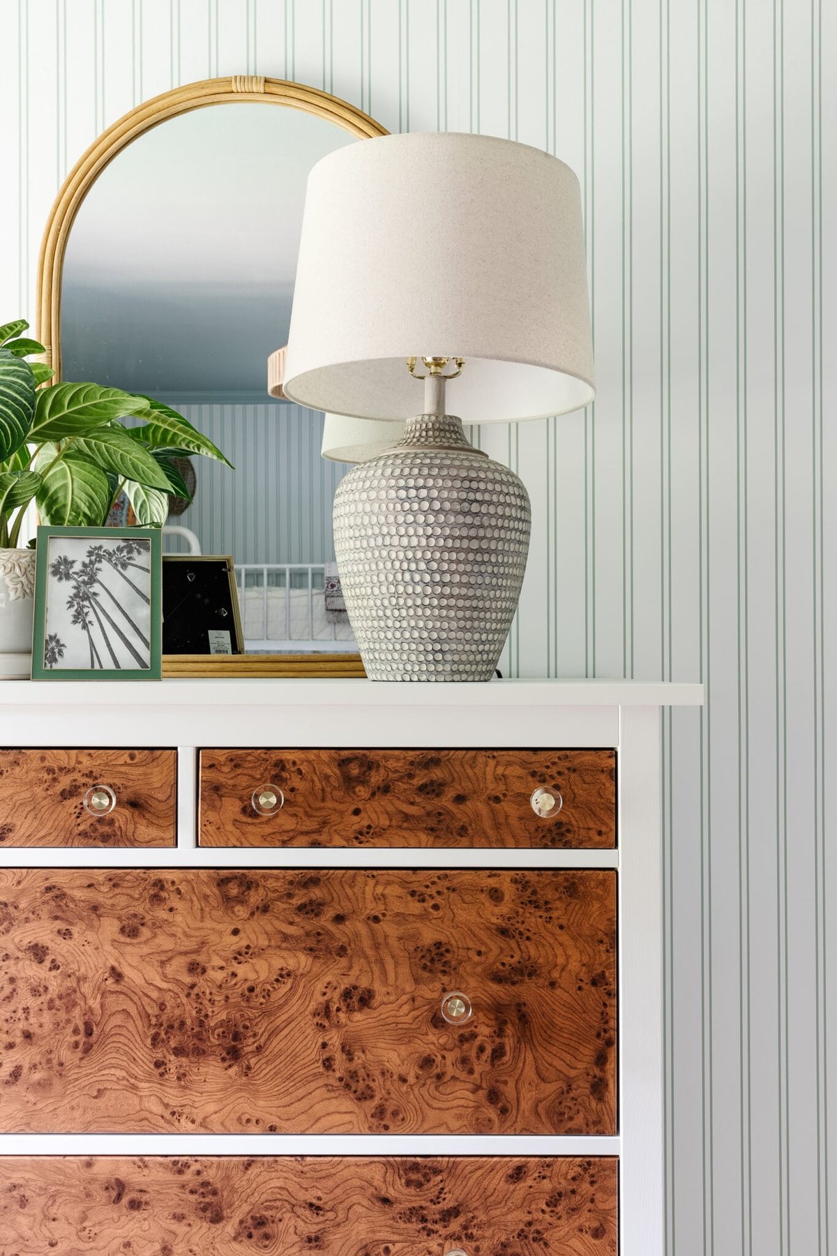table lamp on IKEA dresser with rattan mirror, potted plant, and picture frame