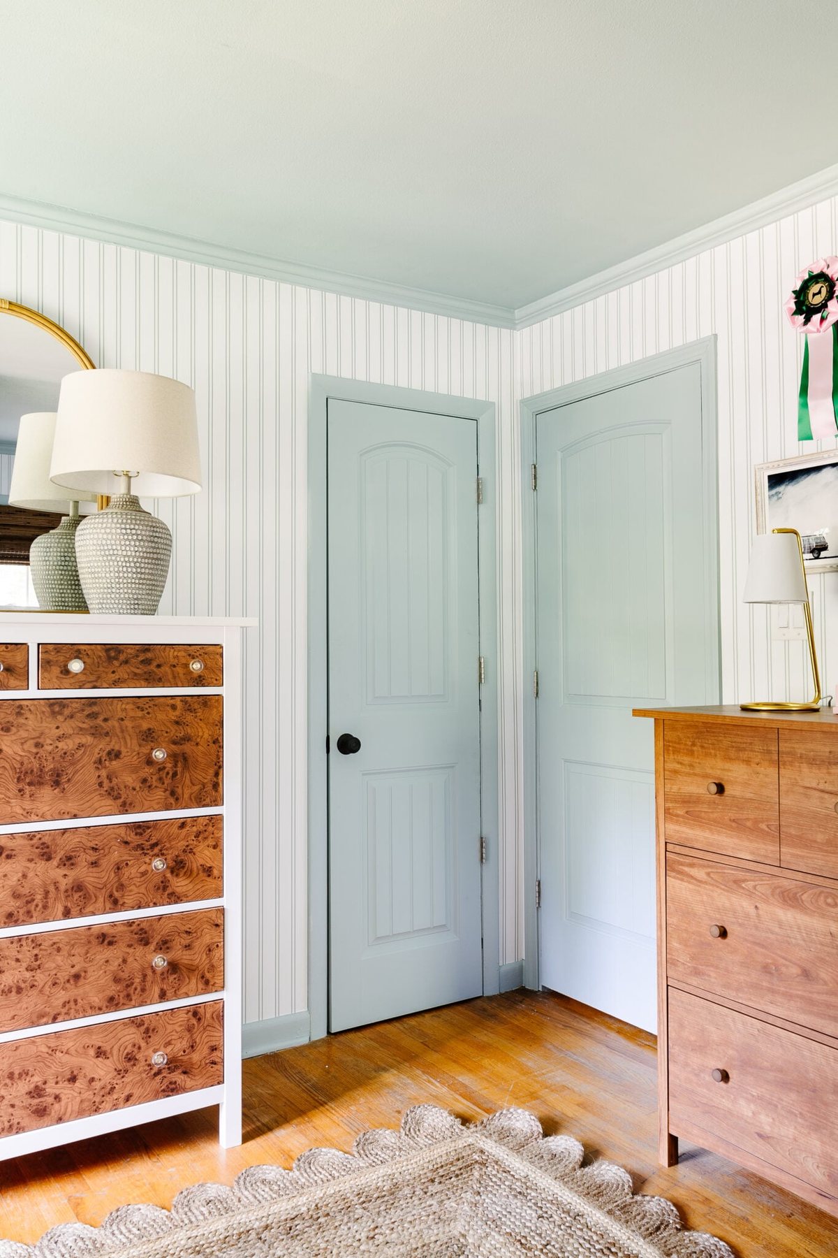 blue doors, trim, and ceiling with striped wallpaper and wooden dressers in shared teenage beach themed bedroom