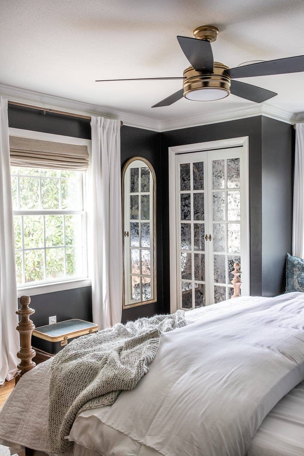 black bedroom with white curtains, mirrored closet doors, ceiling fan, and upholstered wood bed