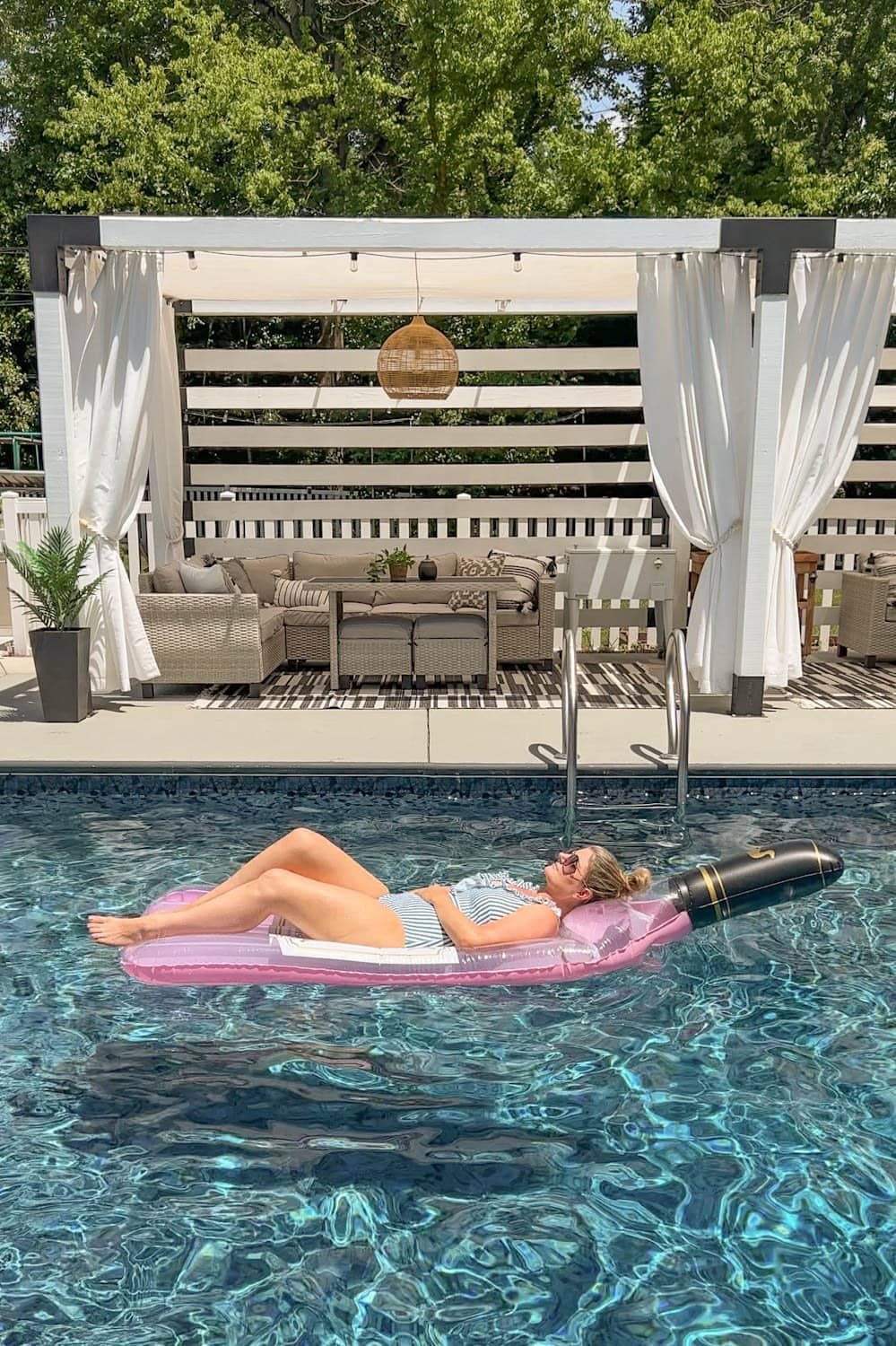 woman lying on a wine bottle shaped pool flat in the water in front of a cabana