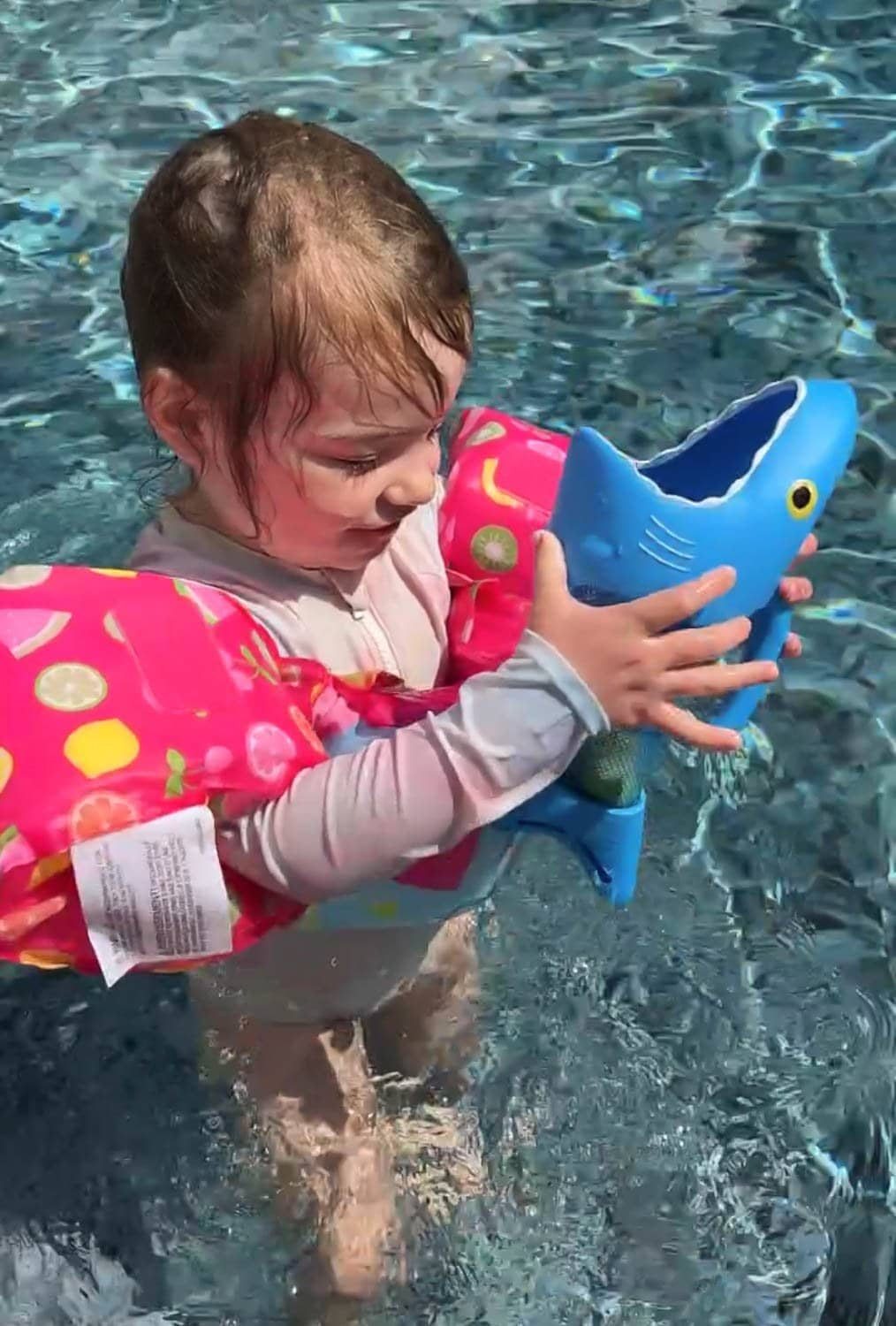 toddler girl playing with a shark pool toy game in the water
