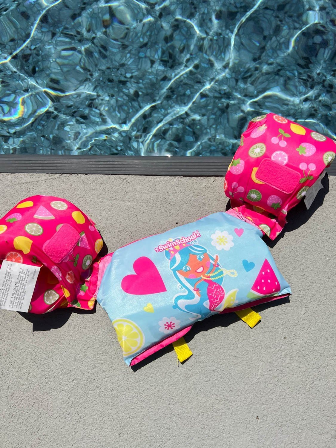 toddler swim vest on the ground on the side of a swimming pool