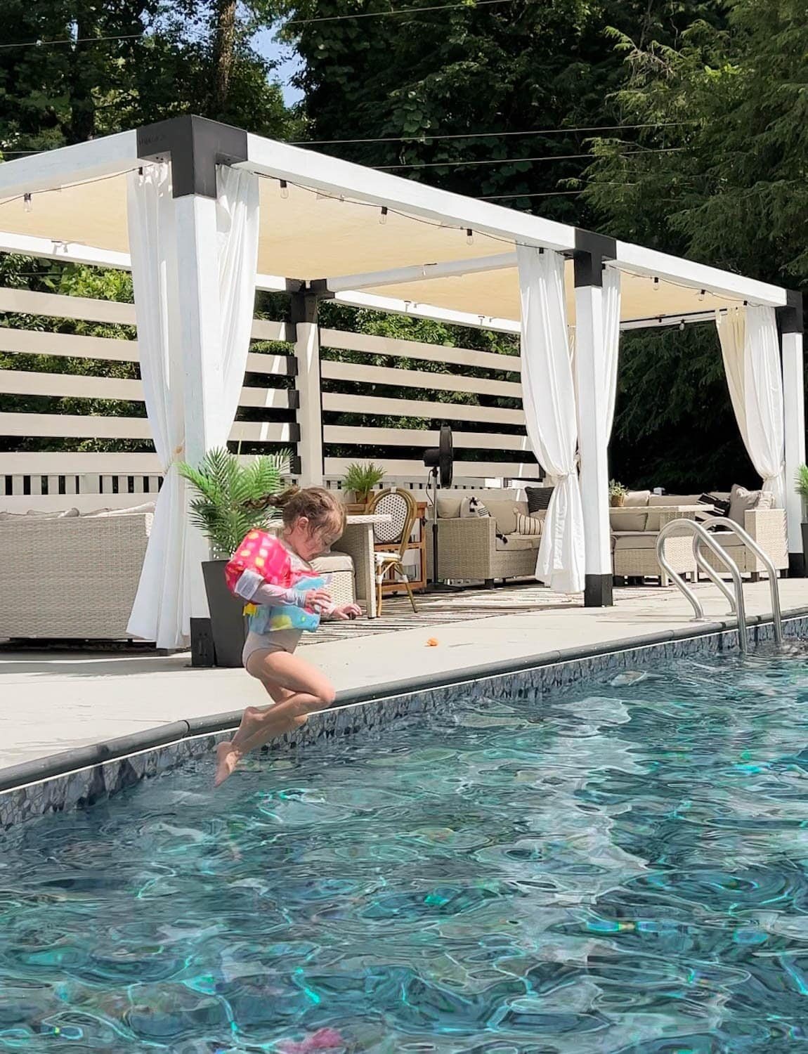 toddler girl jumping into a backyard swimming pool with a vest