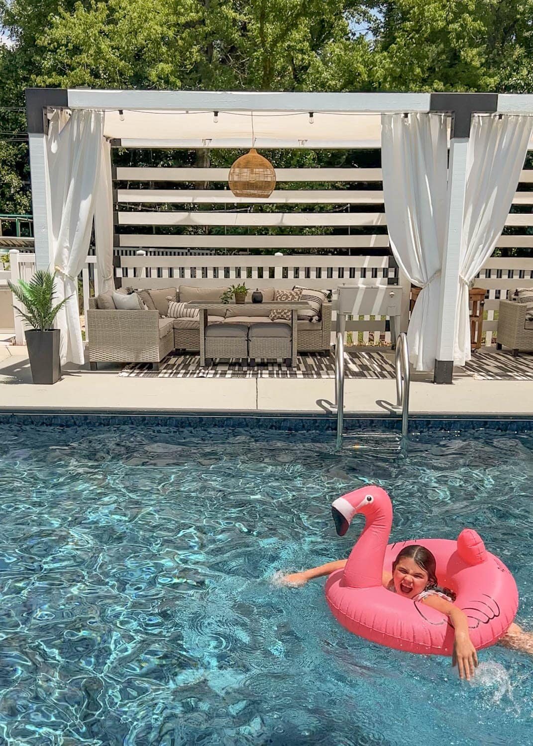 little girl playing on a flamingo pool float tube in the water in front of a cabana